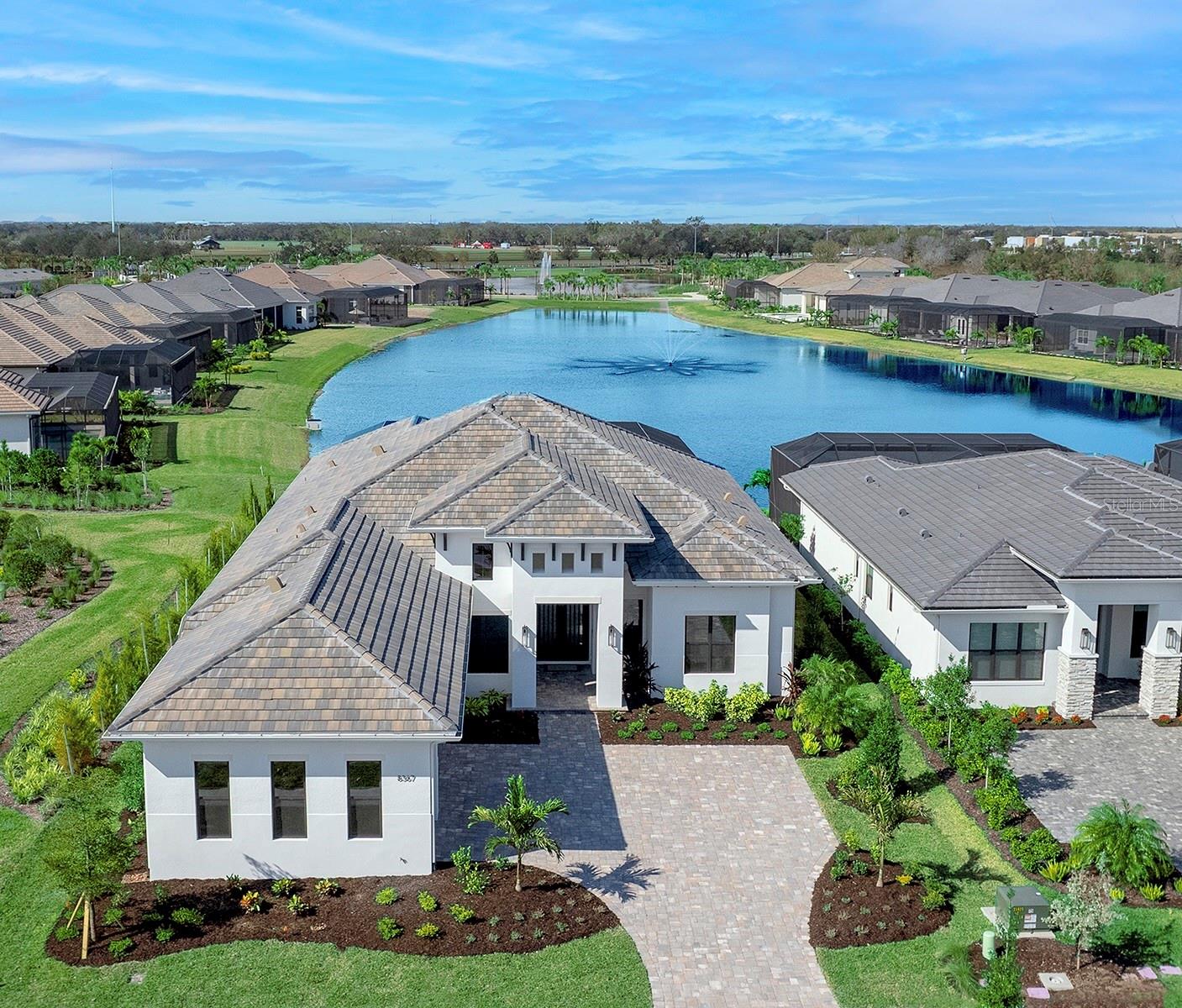 Under contract-accepting backup offers. Just REDUCED $120,000. An amazing value for a Lee Wetherington Home in Wild Blue. Welcome to this stunning new construction custom-built Lee Wetherington home, nestled on a spacious lakefront lot in the prestigious Wild Blue at Waterside in Lakewood Ranch. Revel in the endless, breathtaking water views, complete with a charming lake fountain, and experience the ideal fusion of luxury, comfort, and coastal-inspired elegance. Every detail has been thoughtfully curated to enhance your living experience. Step through the custom iron and glass double doors to discover a home brimming with upgrades rarely found at this price point. The open-concept floor plan boasts 3 bedrooms, 3 baths, large den, and versatile bonus room overlooking the stunning pool area. Designed for seamless living, the great room with a cozy fireplace flows effortlessly into the dining room with a wet bar and the gourmet kitchen, making it ideal for entertaining or relaxation. The kitchen is a chef’s dream, featuring elegant soft-close cabinetry, Cambria quartz countertops and backsplash, an oversized island with a designer light fixture, and premium appliances, including a double refrigerator and built-in ovens. A walk-in pantry adds to the functionality of this space, making it as practical as it is beautiful. Step outside to your private outdoor oasis, complete with Paramount travertine style pavers, a gourmet outdoor kitchen, and two expansive covered living areas. The panoramic screen encloses your saltwater pool and spa, offering serene long water views and a tranquil atmosphere for outdoor enjoyment. The primary suite is a haven of luxury, featuring a spacious bedroom, two large walk-in closets, and a spa-like bathroom with a soaking tub, a walk-in shower, and dual vanities. Your guests will feel right at home in the two additional ensuite bedrooms, each with private bathrooms and walk-in closets. The bonus/theater room is perfect for movie nights or game days, conveniently located near the wet bar. Additional features include a versatile den that can serve as a fourth bedroom, all-impact windows and doors, a large storage room, luxury vinyl flooring throughout, tray ceilings with concealed accent lighting and crown molding, and a 3-car extended garage with epoxy flooring. Experience the Lee Wetherington difference in this exceptional custom home, perfectly positioned on a large lakefront lot in Wild Blue. Schedule your private showing today and step into a life of unparalleled elegance. Wild Blue at Waterside will offer a resort-style clubhouse with over 25,000 square feet of indoor and outdoor space. Indoor amenities include a theater, fitness studio, workout classrooms, golf simulator, locker rooms and more. There’s also wonderful indoor and outdoor dining, a spectacular pool complex with a resort-style pool & lap pool, plus an expansive yoga lawn and premier putting course. To enhance the clubhouse experience, a lifestyle director creates fun and engaging activities to bring friends and family together. Also included is the ALREADY OPEN is the Midway Sports Complex with outdoor pickleball courts, tennis courts, basketball, dog park, sports activity area, great lawn, kayak launch, lakefront viewing and more.