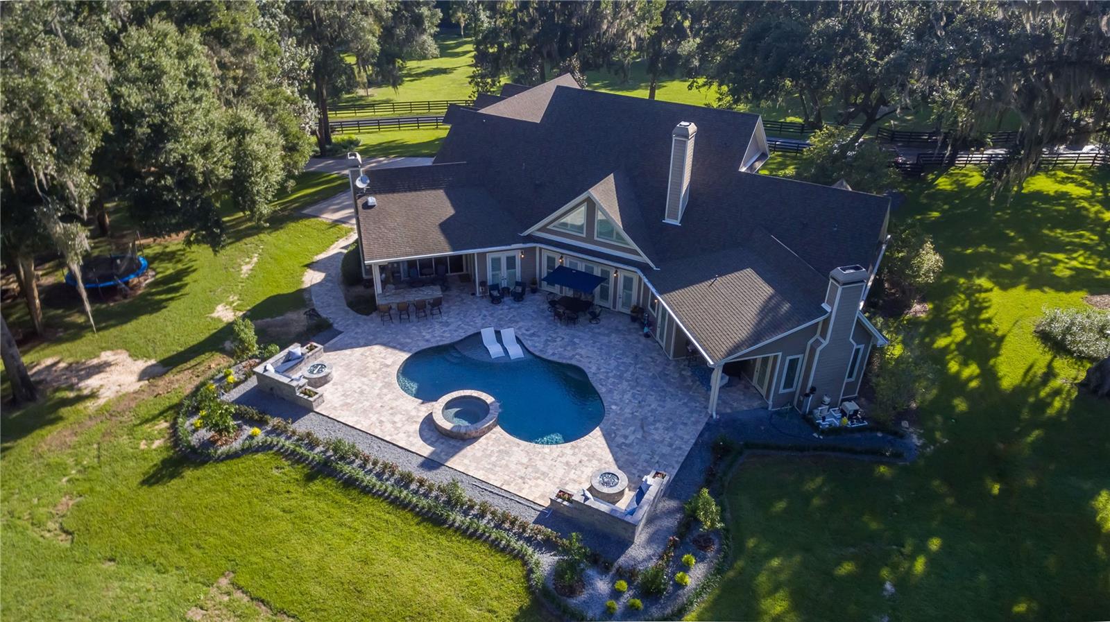 Located in the quiet Shady Hill area, this impressive Central Florida horse farm blends luxury living with equestrian functionality. Set on nearly 5 fenced and gated acres with mature oaks, the property offers a private, park-like setting. The custom-built, two-story main home features 4 bedrooms, 4 full and 2 half baths, showcasing upscale finishes throughout. Interior highlights include soaring ceilings with tray, cathedral, and coffered accents, crown molding, built-ins, and expansive windows with views of the grounds. The chef’s kitchen offers stainless steel appliances, gas range, large center island with breakfast bar, generous cabinetry, and walk-in pantry, opening to a breakfast nook and family room with gas fireplace and French doors to the pool deck. The first-floor primary suite features a gas fireplace, custom walk-in closets, and a spa-style en-suite with dual vanities, walk-in shower, and jacuzzi tub. Upstairs are additional bedrooms, multiple baths, and a versatile bonus room above the garage. Perfect for entertaining, the outdoor living area features a custom saltwater pool and spa, covered lanai with summer kitchen, built-in bar, and multiple fire pits, all complemented by a full lighting system. A detached custom carriage house offers flexible guest or in-law accommodations, easily accessible thanks to a brand new paver walk-way. A full-sized bus garage and 2-bay toy garage is also in-place, offering ample room for extra vehicles of all shapes and sizes. Equestrian amenities include a 2-stall barn with feed room and a large pasture, easily adaptable for additional paddocks. Ideally situated minutes from Florida Horse Park and within 30 minutes of World Equestrian Center (WEC), HITS, OBS, and Ocala International Airport, this exceptional property offers an unparalleled combination of luxury living and equestrian convenience.