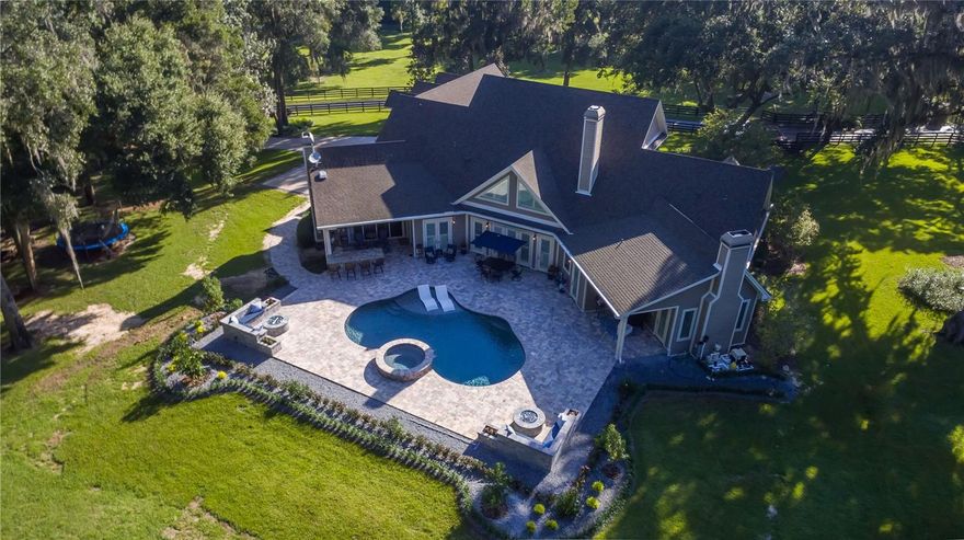 Located in the quiet Shady Hill area, this impressive Central Florida horse farm blends luxury living with equestrian functionality. Set on nearly 5 fenced and gated acres with mature oaks, the property offers a private, park-like setting. The custom-built, two-story main home features 4 bedrooms, 4 full and 2 half baths, showcasing upscale finishes throughout. Interior highlights include soaring ceilings with tray, cathedral, and coffered accents, crown molding, built-ins, and expansive windows with views of the grounds. The chef’s kitchen offers stainless steel appliances, gas range, large center island with breakfast bar, generous cabinetry, and walk-in pantry, opening to a breakfast nook and family room with gas fireplace and French doors to the pool deck. The first-floor primary suite features a gas fireplace, custom walk-in closets, and a spa-style en-suite with dual vanities, walk-in shower, and jacuzzi tub. Upstairs are additional bedrooms, multiple baths, and a versatile bonus room above the garage. Perfect for entertaining, the outdoor living area features a custom saltwater pool and spa, covered lanai with summer kitchen, built-in bar, and multiple fire pits, all complemented by a full lighting system. A detached custom carriage house offers flexible guest or in-law accommodations, easily accessible thanks to a brand new paver walk-way. A full-sized bus garage and 2-bay toy garage is also in-place, offering ample room for extra vehicles of all shapes and sizes. Equestrian amenities include a 2-stall barn with feed room and a large pasture, easily adaptable for additional paddocks. Ideally situated minutes from Florida Horse Park and within 30 minutes of World Equestrian Center (WEC), HITS, OBS, and Ocala International Airport, this exceptional property offers an unparalleled combination of luxury living and equestrian convenience.