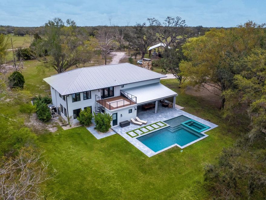 Minutes from the Fruitville Road corridor, take a short scenic drive down canopy roads and arrive at a once-in-a-lifetime farmhouse estate. This country home is among century-old oaks and sits on 18 breathtaking acres. The newly renovated three-bedroom, three-bath, three-car garage home, provides open-concept living with vaulted ceilings, hardwood floors throughout, a wood-burning fireplace featuring a whitewashed stone wall. The crisp and beautifully designed kitchen has a simple aesthetic and boasts newer Café appliances, a center island and composite stone counters and backsplash. Connected to the beautiful kitchen is a spacious walk-in pantry and around the corner, herringbone-laid brick floors enhance the laundry room and side entry door foyer. Cable rail lines the staircase to the second-floor loft, utilized as a home office, but flexible options could be a den, home gym or enclosed for a fourth bedroom. The primary suite is a retreat all on its own, spacious and inviting with two walls of windows overlooking wooded privacy, a generous walk-in dressing room and closet with custom built-ins and glass door cabinetry. The primary bath is a luxurious, inviting space with soaking tub, dual sinks, glass enclosed linen closet and separate shower with marbled porcelain tile. Outside, the best of a country lifestyle continues. In 2023, an inviting new pool and spa was built, surrounded by marble decking and sited next to the lanai with retractable screening. A covered, partially enclosed grill and smokehouse room, makes barbecuing easy come rain or shine. This home is a horse lovers dream. Ramm Flex Fencing around six acres and three pastures was installed 2021, and with a 30-year warranty, it’s practically maintenance free. Two pole barns, one just built in 2022, provide covered storage for equipment and gear, plus two oversized stalls could easily be converted into four stalls and the nearby RV hookup has water and electricity. At the end of a long day, whether you’ve been working the land or working in the office, you will love kicking back here. It’s hard not to fall in love with all this amazing home and land has to offer!