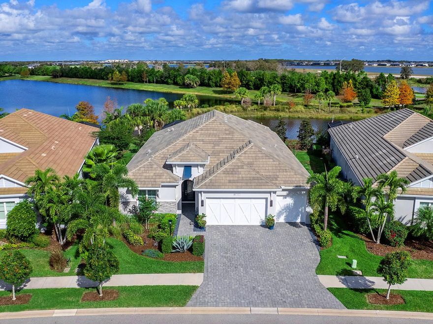 Discover refined coastal elegance and resort-style living in this beautifully upgraded home in Lakehouse Cove at Waterside, perfectly positioned near the community walking path and offering tranquil lake views framed by mature, lush landscaping. A striking coastal front elevation, paver driveway and walkway, and meticulous curb appeal set the tone from the moment you arrive. Inside, a light-filled foyer welcomes you with uplit tray ceilings, a stunning custom glass front door with sidelights and transom windows, textured designer wallpaper, and thoughtful modern upgrades throughout—including upgraded shades on every window and recessed lighting with a nightlight feature. Designed for both comfort and function, the home offers a private guest wing with two spacious bedrooms featuring carpeted floors, tray ceilings, walk-in closets, and generous natural light, along with a stylish shared bath with designer wallpaper, a tub/shower combo, and a storage-rich quartz vanity. Entertain with ease in the dining room, featuring uplit tray ceilings and a dramatic feature wall with a backlit mirror that reflects the great room sliders and amplifies natural light. A dedicated office behind French glass doors provides an inspiring workspace with a tray ceiling, extensive built-in cabinetry, dual seating areas, floating shelving, and quartz counters. At the heart of the home, the chef’s kitchen impresses with abundant perimeter cabinetry, white quartz countertops, a large center island with seating, pendant lighting, a basin sink, stainless hardware, and a full suite of appliances, including a Whirlpool refrigerator, GE Profile dishwasher, GE Profile wall microwave and oven, and a 5-burner GE gas cooktop with vent hood, an Aobosi beverage cooler for cans and wine and a reverse osmosis filtration system. A bright breakfast nook with a chandelier and two pantries adds everyday convenience, while reverse osmosis water at the kitchen sink adds an elevated daily touch. The primary suite is a retreat with a wall of windows dressed in custom draperies, uplit tray ceiling, and tile flooring, while the spa-inspired bath offers dual vanities, including a makeup counter, a large walk-in shower with open entry and tile surround, water closet, linen storage, and a huge walk-in closet with custom built-ins. Outdoor living shines on the paver lanai with a covered seating area framed by columns, ceiling fan and surround sound, plus a chandelier-lit dining space and outdoor kitchen with granite counters, sink, mini fridge, and Bull grill with screened pass-through. Enjoy the oversized pool with a sun shelf, water bowls, and a chaise lounge area, all overlooking the lake through panoramic screening with an ideal northern exposure. The laundry room features abundant cabinetry, folding space, a dry-hanging area, a utility closet, a laundry sink, Whirlpool appliances, and a window. The standard three-car garage offers epoxy floors, overhead storage, and a 240V electric vehicle charger. Additional upgrades include a whole-house generator with transfer switch and a whole-house water filtration and conditioning system. HOA fees include lawn maintenance and 1 Gig fiber optic internet, along with Lakehouse Cove’s resort-style amenities: clubhouse, pool, fitness center, pickleball, playground, walking trails, and a water taxi stop to Waterside Place. Minutes to downtown Lakewood Ranch, UTC Mall, the new Mote Aquarium, Sarasota Polo Club, golf, and Sarasota’s Gulf beaches.
