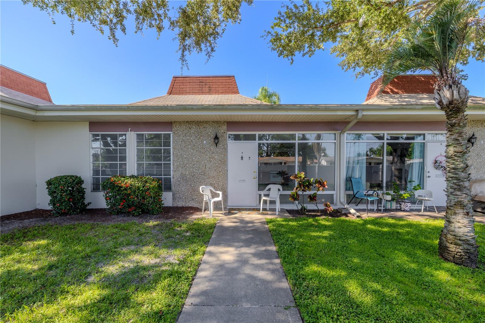 Welcome to this clean, well-maintained 2-bedroom, 1-bath condo in the desirable 55+ community of Tahitian Gardens in Holiday, Florida. With a NEW HVAC system installed in July 2025, this move-in-ready unit offers easy, low-maintenance living in a vibrant, amenity-rich neighborhood.
The exterior features a welcoming front patio, ideal for enjoying a morning coffee or an evening breeze. A paved walkway leads to the entry, bordered by manicured landscaping and mature shrubs. Large front windows allow for great natural light and courtyard views, while a textured accent wall adds subtle architectural character.
Inside, you'll find a bright and open floor plan that combines the living, dining, and kitchen areas into one versatile space. Freshly painted walls and neutral flooring give the unit a clean, modern feel. The vintage-style kitchen stands out with its nostalgic turquoise appliances and warm wood-look cabinetry—plenty of storage and personality included. A ceiling fan adds function and charm.
The main living area is open and spacious, featuring a full wall of windows that flood the space with light and a pleasant view of the landscaped common area. The layout allows for flexible furniture arrangements to suit your lifestyle—whether it's a cozy living area, dining setup, or workspace.
The primary bedroom is light and spacious, with a large picture window that offers more natural light and a green view. It has two large closets. Bedroom 2 is similarly bright and functional, featuring a spacious closet and ample room for guests or hobbies.
The bathroom features a practical layout with ample counter space, vintage wood cabinetry, and a tub-shower combo complemented by classic tile that extends to the ceiling. A built-in shower seat and grab bar provide extra safety and convenience.
Tahitian Gardens is a well-maintained, active 55+ community with numerous amenities, including a heated pool, shuffleboard, walking paths around a scenic lake, and a diverse range of clubs and social events—from arts & crafts to card games. Just 3.8 miles to Fred Howard Park and the Gulf beaches of Tarpon Springs, and within strolling distance to CVS, Walgreens, Aldi, and public transit. Tampa and Clearwater airports are within an hour's drive.