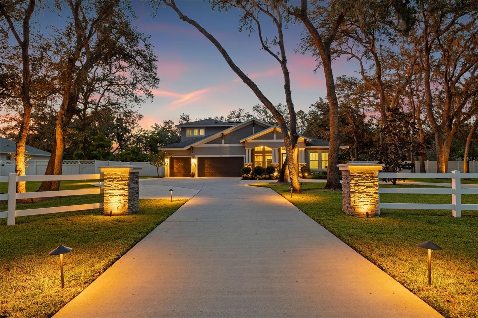 This stunning 2019 Cardel-built home sits on a fully fenced 1.25-acre lot and features 5 bedrooms, 4 full baths, a dedicated office, a huge bonus room, and an incredible resort-style heated, salt water pool and spa. As you enter through the charming white fence, and around the circular driveway, the home's curb appeal immediately impresses with stone-wrapped columns and an inviting front porch. Inside, the open floor plan is accentuated by soaring 12-foot ceilings, elegant crown molding, and 8-foot doors, all centered around a spacious family room with a dramatic stone accent wall and electric fireplace. Just off the entryway, French doors open to a private office, perfect for working from home. The crown jewel of the main level is the expansive primary suite, privately tucked away for serenity and comfort. This luxurious retreat offers stunning views of the pool and backyard through large windows, and features a tray ceiling, ample space for a sitting area, and a built-in desk or vanity nook. The spa-like en-suite bath includes a walk-in shower, freestanding soaking tub, dual vanities, and a large custom walk-in closet. There are three additional, spacious bedrooms on the first floor. The open-concept kitchen is designed for entertaining, with a generous island, sleek stainless steel appliances, white cabinetry, stone countertops, a large stainless sink, stylish lighting, and a spacious walk-in pantry. Upstairs, you’ll find the fifth bedroom and a massive bonus room, perfect for a home theater, game room, or guest suite, complete with its own full bath. The true highlight of this property is the incredible lanai with spectacular Nebula lighting, a resort-style pool and huge fenced backyard. The brick-paver pool deck features a show stopping sparkling salt water pool and spa including a waterfall grotto with built in bench, a sun shelf and in-pool umbrella, all surrounded by lush tropical landscaping. There is an ample amount of covered seating for outdoor dining and entertaining, along with a built-in outdoor kitchen/ grill area. Additional features include a Whole House Generator, large storage shed, and fabulous landscape lighting. With no HOA restrictions, there’s room to bring your boat, RV, or recreational toys—making this home the ultimate blend of luxury living and laid-back Florida lifestyle.