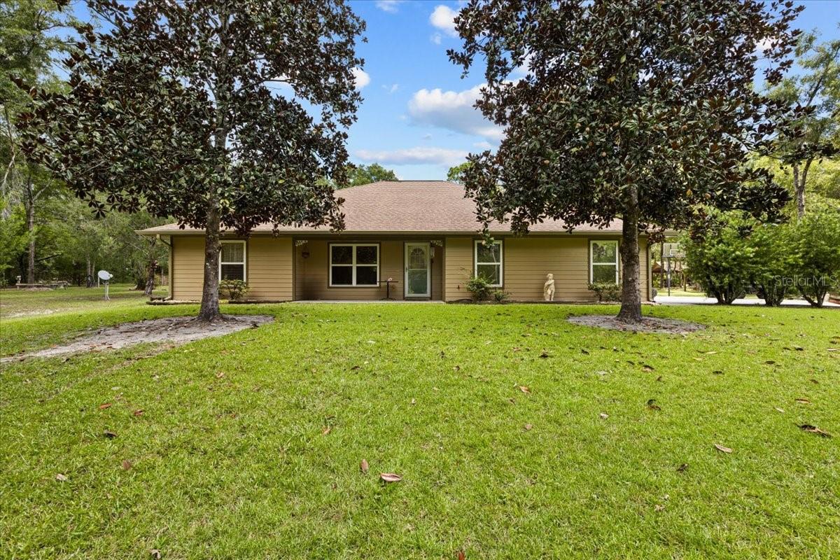 PRIVACY and BEAUTY abound at this 9.39 ACRES on a PAVED road just north of Bell, in the Rock Bluff area. Enter the property thru a brick column, iron gate driveway that winds to the custom 3 BD/2 BA CONCRETE BLOCK home also has hardiplank siding making it stronger and giving better insulation. The spacious home boasts 1,441 SF of living area and has a large covered back porch and attached garage, making 2,322 SF under roof. The split plan home offers 2 large bedrooms on one end of the home with bathroom between that has a 1920 antique pedestal sink. The Master Bedroom, with a private french door access to the back porch, has a nice walk-in closet and master bath with double sink vanity and walk in shower. The open concept living, dining, kitchen area is light and bright! The kitchen has an abundance of cherry wood cabinets and a prep sink, in addition to the double sink. The Corian countertops are maintenance free and durable. There is a pantry closet, next to the laundry closet, for added storage. A pleasant surprise at this property are the added buildings outside! A 12'x20' GUEST COTTAGE/"SHE SHED" is cute as can be with its front porch! A small kitchen area and bathroom and open living/sleeping area make it so convenient for guests. Another utility building with 2 wings is great storage for almost anything! In addition, there is another LARGE 36'x44' POLE BARN with concrete floor and includes a 15'x18' WORKSHOP. There is an air compressor installed and piping runs throughout the barn and workshop. Another 12'x36' wing of this pole barn has limerock floor. Toward the back of the property, yet another pole barn (16'x20') is situated for parking boats, trailers, or any other items you may need to store. The owner has taken meticulous care of the property. Upgrades include a new HVAC unit June 2025, water system 2024, gutters added 2020. Call to set up your private tour today!
