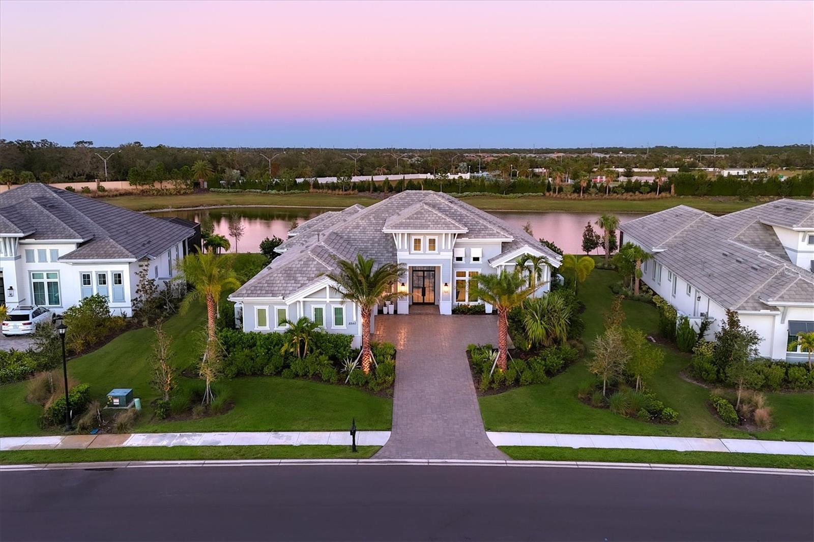 Welcome to 8540 Pavia Way in the Lake Club of Lakewood Ranch. This home is being offered furnished. This Gardenia II floor plan. 4,000 square feet of living space, offering four bedrooms and 4.5 baths. As you enter through the grand foyer, a soaring ceiling and the custom glass front door and transom window set the tone. Del Ray Alaska matte porcelain flooring leads through the main living areas. The great room impresses with a voluminous designer ceiling and chandelier, custom niches and pocketing sliders with designer draperies. The kitchen features a large floating island with quartz countertops and seating, a spacious walk-in pantry with wood shelving, and JennAir stainless-steel appliances, including a gas cooktop, vent hood, and built-in oven and microwave. A subway tile backsplash with custom cabinetry and under-cabinet lighting complements the quartz countertops. The formal dining area features a dry bar with a wine cooler, custom cabinetry and a quartz countertop. The main living spaces seamlessly connect indoor and outdoor living. The travertine lanai is an oasis with a no-see-um panoramic screen showcasing a serene lake view framed by lush landscaping and accent lighting. The outdoor kitchen is designed for gatherings, featuring bar-height seating, a grill, a vent hood, cabinetry with a tile backsplash, granite countertops, a beverage cooler and a prep sink, enhanced by a tile fireplace, with a mantle and wide-format shiplap. The lanai also has remote-controlled Storm Smart screens for peace of mind. The heated saltwater pool and spa with autofill and overflow drain complete the lanai. The primary suite is a grand sanctuary with an alcove entry and double doors. This serene retreat boasts a custom tray ceiling and a designer chandelier, a seating area, and glass French doors with glass panel sides and custom draperies that lead to the lanai. The spa-like primary bath features a soaking tub, a large walk-in shower, dual vanities with quartz countertops, and a water closet with a Toto toilet. Two walk-in closets with custom built-ins provide ample storage. The den, with French glass doors and a picture window, provides an ideal workspace. The bonus room is complete with a designer tray ceiling, sliders and versatile potential as a gym, game room or media room. Three well-appointed guest suites feature custom-designed tile in the showers and beautiful vanities with stone countertops, and each has a walk-in closet. One of the guest en-suite baths also doubles as a pool bath. Additional highlights include a half bath with a custom vanity that has a tick-edge stone countertop, a spacious laundry room with quartz countertops with folding space, subway tile backsplash, a sink, a window and abundant cabinetry, and a three-car garage featuring an epoxy floor. This home showcases premium upgrades, including hurricane-rated windows and doors, a whole-house generator, a water filtration system, a reverse osmosis kitchen sink filter, a whole-home scent system, tinted front windows, a Sonos sound system and a professionally sealed oversized driveway. The Lake Club has a wealth of amenities, including two resort-style heated pools, a clubhouse with fine dining and bar area, a fitness center, spa, tennis courts, pickleball, a playground, dog park, and a full-time concierge and activities director. Additionally, residents are near The Mall at University Town Center, Lakewood Ranch Main Street, Waterside Place and numerous dining options.