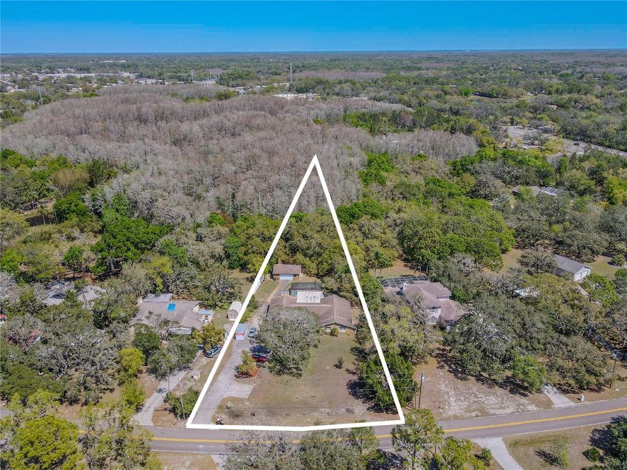 Welcome to your private Florida retreat. Tucked away on 1.27 fenced and shaded acres, this 4-bedroom, 3-bath pool home in Port Richey offers the best of both worlds—room to breathe and live life your way, yet minutes from shopping, dining, and major highways. With no HOA or deed restrictions, you have the freedom to park your RV or boat on-site, bring your toys, and truly make the property your own. From the moment you arrive, the long driveway and detached two-car garage with built-in workbench set the tone for both practicality and possibility. A brand-new roof (August 2025) means peace of mind for years ahead. Inside, the home strikes a perfect balance of warmth and functionality. Double front doors open to a tiled foyer with beveled glass and a wrought-iron accent, welcoming you into the spacious living and dining area. At the heart of the home, the kitchen and family room shine with vaulted ceilings, exposed wood beams, a cozy stone fireplace, and an open flow that makes gathering easy. The kitchen boasts solid wood cabinets with crown molding, granite counters, stainless-steel appliances, and a breakfast bar complete with wine rack. A massive 26-foot-wide bonus room with French doors to the lanai offers endless possibilities—home office, gym, playroom, or game room. Step outside, and the saltwater pool feels like your own private resort, tucked beneath the shade of mature trees and framed by a screened enclosure and covered patio with ceiling fans. The primary suite includes dual walk-in closets, wood-look laminate flooring, and direct lanai access. Its ensuite bath was refreshed in 2025 with new lighting and paint and features a granite-topped double vanity, step-in shower, and plumbing already in place for a future soaking tub. Two additional bedrooms share another refreshed full bath, while the fourth bedroom enjoys its own fully renovated bathroom with a soaking tub and rain shower. A full laundry room with sink and cabinets adds everyday convenience. The backyard is fully fenced and shaded—perfect for pets, gardening, or simply enjoying the peace and quiet. And when you’re ready to explore, you’re just minutes from Werner-Boyce Salt Springs State Park, Jay B. Starkey Wilderness Park, and a short, commutable drive to Tampa via the Veterans Parkway or US 19. This home is more than just a place to live—it’s a lifestyle. With its land, flexibility, and recent upgrades, it’s a rare find in today’s market. If you’ve been searching for space, freedom, and comfort, this is the one.