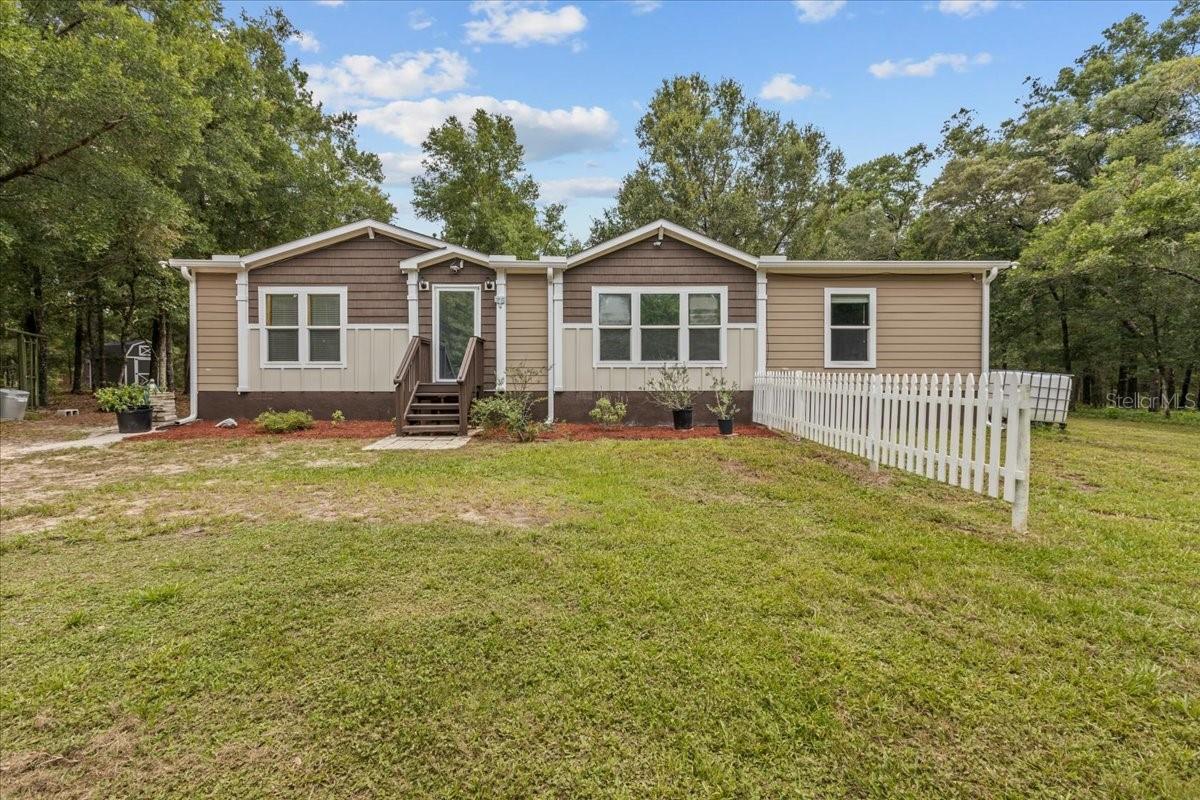 Welcome to your private paradise! Nestled on 4.69 beautifully fenced acres, this 2018 upgraded 3-bedroom, 2-bathroom home offers the perfect blend of comfort, charm, and countryside living— Escape the hustle without sacrificing convenience. Located only 20 minutes of Gainesville, over the county line, where you can take advantage of the lower Levy county taxes. Step inside this 1,456 sq ft home and feel instantly at peace with its warm, earthy tones and custom details throughout. Thoughtfully upgraded, the home features 2x6 exterior wall framing, stucco skirting, gutters and downspouts, and sheetrock walls throughout for a polished, modern feel. A brand-new Carrier air conditioner (installed May 2024) and a newer well pump (2020) ensure comfort and reliability year-round.The open floor plan is designed for easy living and entertaining, with ample built-in storage and shelving throughout. The kitchen is a chef’s delight, boasting stainless steel appliances, a gas range, and a center island with granite countertop—perfect for meal prep or casual dining. A spacious laundry room includes an additional refrigerator and built-in counter space, ideal for folding or extra pantry storage.Retreat to the luxurious primary suite, featuring an oversized bathroom complete with double vanities, abundant cabinetry, a soaking tub, and a beautiful, extra-large walk-in shower. Both spare bedrooms offer walk-in closets and additional storage. Outside, the property is equally impressive. Enjoy three storage sheds, a freshly painted 40-foot high-cube shipping container, two chicken coops, and three fenced-in garden areas ready for your green thumb.Nature lovers and homesteaders will appreciate the 17 Arbequina olive trees, known for being self-pollinating and producing antioxidant-rich olives ideal for oil. Additional plantings include sugarcane, a key lime tree, a lemon tree, native paw paw trees, beauty berry shrubs, and yucca plants.If you are looking for a peaceful retreat or a space to roam, this one-of-a-kind property offers the freedom and tranquility of country living with the convenience of city access and lower taxes. A low annual Property Owners Association Fee of $32.04 a month. Schedule your showing today and come experience the lifestyle you’ve been dreaming of!