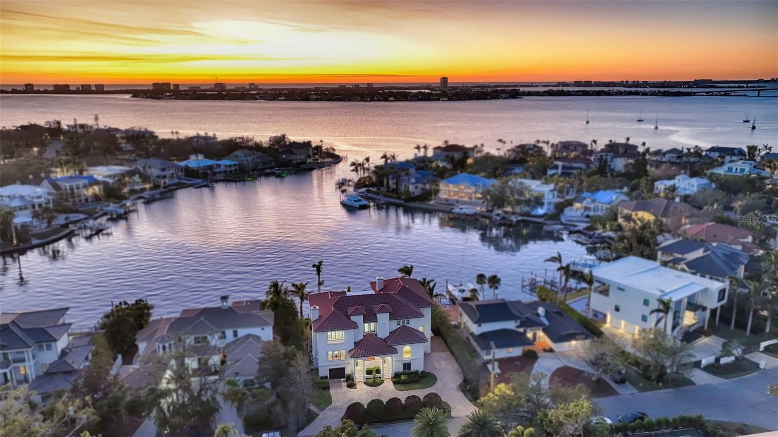 Harbor House, located at 1430 Harbor Drive, stands as the crown jewel of Harbor Acres, Sarasota’s most coveted mainland neighborhood known for record-breaking sales year after year. This extraordinary waterfront estate, spanning over 12,000 total sq. ft., exemplifies impeccable craftsmanship and design. Completed in 2023, the home was reimagined to offer over 7,000 air conditioned sq. ft. of professionally curated luxury living, appealing to the most discerning tastes. Entering through the grand foyer, you are greeted by 25-foot ceilings, a double-tiered crystal chandelier, and walls of two-story windows that frame breathtaking westward views of Sarasota Bay. From here, step onto the expansive covered veranda with its summer kitchen and grill, perfect for dining, entertaining, or simply soaking in the serene waterfront setting. The home showcases exquisite craftsmanship with marble and American walnut floors, custom cabinetry by Campbell’s Custom Cabinetry, and 12-inch crown moldings throughout. Designed to be as inviting as it is opulent, the walnut-clad library offers a warm retreat for meetings, reading, or quiet evenings. Every detail has been thoughtfully executed, including hurricane-impact metal-framed windows and doors, anti-glare UV technology, and electric blinds to enhance comfort while maintaining mesmerizing water views. The banquet-sized kitchen is a chef’s dream, featuring a professional-grade 60-inch gas range, cocktail bar, stone-framed fireplace, and spacious dining and lounge areas. It opens seamlessly to the family room, ideal for gatherings and game-day celebrations. The grand salon, with its 11-foot ceilings, custom woodwork, and gas fireplace, exudes sophistication, while the formal dining room is perfect for entertaining, adjacent to a 1,100-bottle wine room and a scullery with wine bar and warming drawer. Upstairs, a curved staircase leads to a gallery overlooking the foyer and three guest suites, each with private balconies and en-suite marble baths. The owner’s suite, occupying the entire north wing, offers a private retreat with a gas fireplace, a spa-like bath, a custom wardrobe room designed for over 100 pairs of shoes, and an 18-foot covered balcony with panoramic bay views. The outdoor oasis includes 110 feet of deepwater frontage, a private dock, a saltwater lap pool, spa, and an expansive entertaining terrace with a TV. The ground floor offers 3,684 sq. ft. of additional space, including four garages, play areas, and storage, all serviced by an elevator connecting all three levels. Nestled in the premier Harbor Acres neighborhood, Harbor House is both a welcoming home and an entertainer’s dream, just minutes from downtown Sarasota.