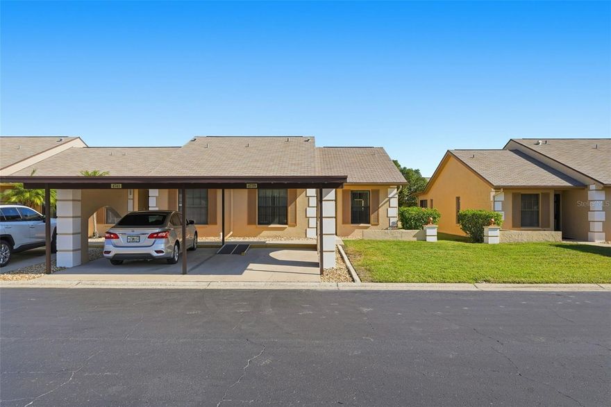 Welcome to this charming 2-bedroom, 2-bathroom villa-style condo located in the desirable 55+ community of Bay Park Estates in Holiday. This end-unit home offers exceptional privacy and convenience in a bright, open layout perfect for easy Florida living. Step under your covered carport and walk right into an inviting open floor plan. The kitchen sits to your right, featuring a stainless steel refrigerator and stove, an abundance of cabinetry, and a convenient coffee bar or prep station. The living and dining room combo boasts vaulted ceilings, creating a spacious, airy feel, and natural light flows throughout the home. Ceiling fans in every room ensure comfort year-round. The split floor plan offers ideal privacy. The primary bedroom includes a large walk-in closet with built-in organizers and an ensuite bathroom featuring a generous vanity, glass-enclosed shower, and a linen closet. The second bedroom is comfortably sized, with the guest bathroom offering a shower/tub combo. Enjoy the convenience of an in-unit washer and dryer closet, and relax on the enclosed back lanai, perfect for enjoying peaceful views and Florida weather any time of year. An additional storage closet on the lanai provides even more functionality. Roof maintenance is handled by the HOA, giving you peace of mind. Bay Park Estates offers wonderful amenities, including a community pool and shuffleboard courts, and is ideally located close to shopping centers, grocery stores, and dining options. Move right in and start enjoying the relaxed, maintenance-free lifestyle you’ve been looking for! Schedule your showing today!