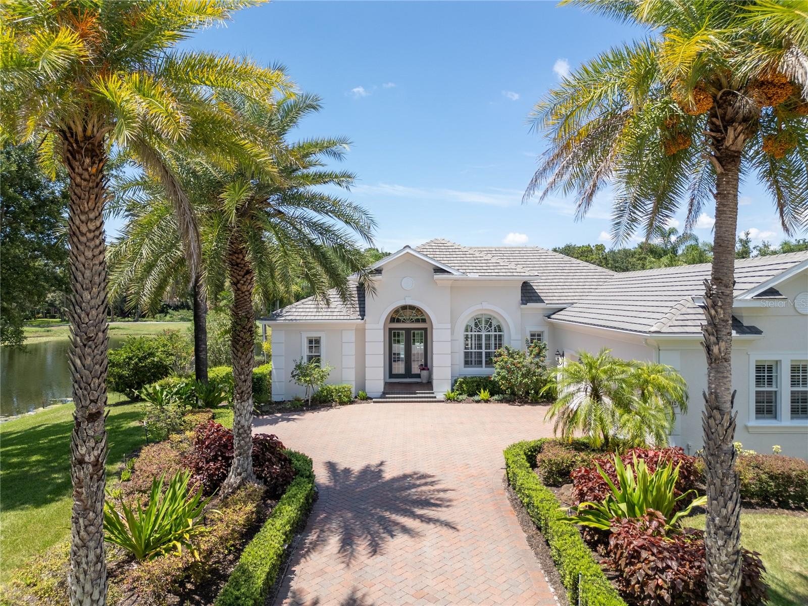 Welcome to one of the most captivating homes in the gated enclave of Lakewood Ranch Country Club, perfectly positioned with water on two sides and stunning views of the picturesque 5th hole on the King’s Dune golf course and the brilliant sunsets from the lanai are not to be missed. This timeless residence blends privacy, sophistication, and comfort in one of the most sought-after golf course communities on Florida’s Gulf Coast.
From the moment you step through the grand double doors, you’re greeted by soaring ceilings, detailed crown molding, and expansive windows that flood the home with natural light. The open-concept living spaces are thoughtfully designed for everyday elegance and effortless entertaining. At the heart of the home, the chef’s kitchen impresses with rich solid wood cabinetry, sleek quartz countertops, high-end appliances, a wine room, and a breakfast nook that overlooks tranquil lake and fairway vistas.
Freshly painted, this home features impact-rated glass throughout and updated flooring, kitchen, bathrooms, lighting, new outdoor kitchen with new grill and mini refrigerator, and feature TV wall surrounded by stunning distinctive walls of shiplap wood trim. The water heater and pool heater have also been replaced in 2025.
Step outside to your private retreat—an oversized lanai with multiple seating areas, an outdoor kitchen, and a saltwater pool and spa, all framed by lush tropical landscaping and stunning sunset views over the water.
The owner's suite is a true sanctuary featuring a tray ceiling, beautiful natural light, and an oversized spa bath with a walk-in shower, soaking tub, and dual vanities. Two comfortable guest bedrooms, a den with custom built-ins, and a formal dining room offer flexibility and function. Additional features include a spacious laundry room, air-conditioned storage off the garage, and designer lighting throughout.
Set within the heart of Lakewood Ranch, the Country Club neighborhood offers miles of scenic trails, parks, and optional membership to four championship golf courses, world-class tennis, pickleball, fitness, and vibrant social activities. Just minutes from Lakewood Ranch Main Street, Waterside Place, shopping, dining, and award-winning Gulf beaches.
This is more than a home—it’s a lifestyle. Schedule your private showing today.