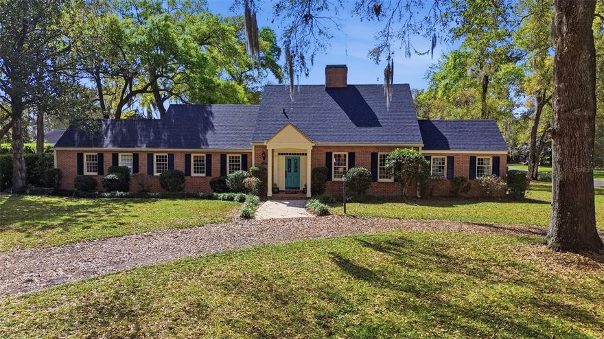 If you’re someone who appreciates a home with character and space to spread out, this one might be calling your name. This 4-bedroom, 3.5-bath brick home sits on over half an acre and blends old-school charm with thoughtful modern updates throughout.
Pull into the circular driveway and step inside where the original wood floors immediately set the tone. To the right, the living room welcomes you in with a cozy wood-burning fireplace and flows naturally into the dining room, which wraps around to the kitchen, making the layout feel both connected and comfortable for everyday living or entertaining. The kitchen is full of personality and practicality. A built-in brick cooking area with a gas stove and wall oven becomes a standout feature, while the generous counter space and breakfast bar with high-top seating make it easy for everyone to gather. And if storage is high on your wish list, the massive built-in pantry might just steal the show. Just off the kitchen is a bright sunroom with brick flooring and tons of natural light. The kind of space that makes your morning or evening lounging time feel a little extra special. Tucked off the sunroom is the laundry room with a convenient half bath, perfectly placed for quick trips inside after enjoying the pool out back.  Wooden ceiling beams carry through into the den/family room, giving the space feel like “old meets new” vibe. You have multiple built-in shelves with another wood burning fireplace. Down the hallway you’ll find a bedroom with two built-in closets, one of them cedar-lined, along with the spacious primary bedroom featuring built-in shelving, a walk-in closet, and an ensuite bath. Head upstairs and the original wood floors continue into two additional bedrooms and a full bath, offering plenty of room for a growing family, guests, or that “finally getting my own space” teenager. Out back, the pool and brick patio create a great spot for grilling, relaxing, or soaking up some Florida sunshine. With the oversized lot you get a little breathing room while still being tucked away from the main roads, yet close enough to downtown to run errands without turning it into a whole-day adventure. In short: character, charm, space, storage, and a pool to top it off. Not a bad combo.