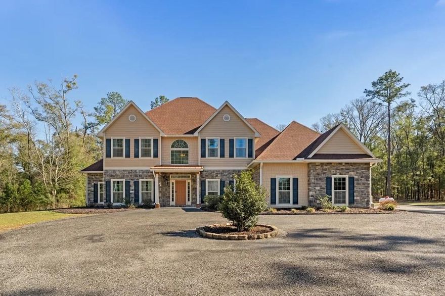 Welcome home! Recently appraised at $925,000, this 2019 custom-built estate in the gated Grand Oaks community offers exceptional space, privacy, and value on 2.97 wooded acres just minutes from I-75. Sellers are motivated and ready to review strong offers. With nearly 4,500 square feet of heated living space (over 5,700 under roof), the home features 4 bedrooms, 3 full baths, 2 half baths, a main-level primary suite, an upstairs suite, two additional guest rooms, a loft, private theater, two offices, and multiple living areas, ideal for both everyday living and entertaining. The open great room showcases soaring ceilings with wood beams, a stone gas fireplace, and abundant natural light. The chef’s kitchen is equipped with custom cabinetry, quartz countertops, a large island, and stainless steel appliances. Enjoy peaceful wooded views from the covered back porch with plenty of room to design your dream outdoor retreat. Hardwood floors, surround sound, and an oversized garage complete this impressive property.