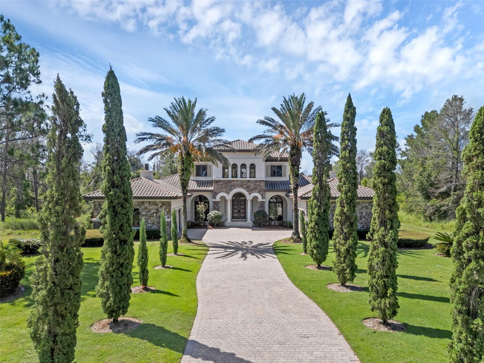 Sophisticated luxury in Bella Collina's Premier Golf Community, sits this exquisite estate, a true masterpiece of luxury living. Spanning over 6,500 square feet and situated on nearly 1.5 acres of impeccably landscaped grounds, this residence offers an unmatched blend of elegance, privacy, and resort-style amenities — including a breathtaking, oversized custom pool. Designed for those who appreciate the finer things, the home features 4 expansive bedrooms, 4 full bathrooms, 2 half baths, a private home office, a media room, and a spacious 4-car garage. Every room is thoughtfully positioned to take full advantage of panoramic views of Bella Collina’s lush surroundings. As you approach, a grand driveway framed by manicured gardens sets the tone for what lies beyond. Inside, soaring ceilings, newly installed hardwood floors, oversized windows, and a show-stopping chandelier create a dramatic and welcoming entrance, with unobstructed views of the pool and grounds drawing your eye from the moment you step inside. The main level is a seamless blend of form and function. The gourmet kitchen is a chef’s dream, outfitted with premium stainless steel Wolf appliances, a Lacanche range, custom cabinetry, Calacatta gold marble countertops, designer backsplash, a gas cooktop, and two oversized islands—ideal for both entertaining and culinary creations. Just off the kitchen, a warm and inviting family room features an elegant fireplace, custom coffered ceilings, and floor-to-ceiling sliding doors that extend the living space outdoors. Also on the main floor is the luxurious owner’s suite—an elegant retreat with a cozy seating area, serene natural views, dual walk-in closets, a lavish en-suite bath with soaking tub, dual vanities, Calcutta gold marble countertops, walk-in shower, private laundry, and a versatile flex space ideal for a gym, nursery, or additional office with a hidden features. The main level also includes a formal dining room with its own wine cellar, a guest suite with private bath, and a large laundry room with ample storage Upstairs, rich hardwood flooring continues throughout, leading to an oversized loft with built-in cabinetry, a formal sitting area, and picturesque views of the property. Two generously sized bedrooms, each with walk-in closets and luxurious en-suite baths featuring quartz countertops and designer tile finishes, complete the upper level. Outdoors, the covered lanai spaces are perfect for entertaining year-round, offering an outdoor kitchen, fireplace, and multiple seating areas. The oversized resort-style pool with spa creates a tranquil escape for relaxation or entertaining under the Florida sun. Residents of Bella Collina enjoy access to world-class amenities, including a championship Sir Nick Faldo-designed golf course, a Tuscan-inspired clubhouse with two restaurants, spa, fitness center, tennis courts, resort-style pool with cabanas, and scenic walking trails. The community also offers a private boat ramp, dog park, and 24-hour manned security for peace of mind. Ideally located with convenient access to major highways, this estate offers proximity to top-rated schools, elite medical facilities, luxury shopping, fine dining, and world-renowned theme parks. This exceptional property presents a rare opportunity to experience the pinnacle of luxury living in one of Central Florida’s most prestigious communities. Schedule your private tour today.
