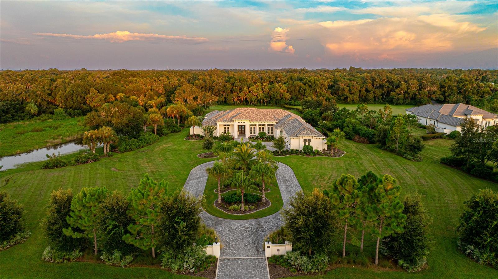 Welcome to an extraordinary estate in the heart of Sarasota, Florida. Set on just under five acres of lush, landscaped grounds, this remarkable property offers the perfect blend of modern sophistication and serene privacy. With over 4,500 square feet of meticulously designed living space, this four-bedroom, four-and-a-half-bath home is a true masterpiece of contemporary elegance. As you approach the home, the grand tile roof and stunning facade makes an immediate impression. Step inside to be greeted by an open floor plan that exudes warmth and modern charm with vaulted ceilings with exposed beams along with a coffered ceiling in the kitchen creating an airy, expansive feel, while the home's stunning interior lighting casts a welcoming glow throughout. The true gourmet kitchen, designed for both the avid chef and the casual entertainer features a massive island with ample seating, a gas range, a commercial-sized fridge and freezer, and a walk-in pantry, this kitchen is as functional as it is beautiful. The open layout flows seamlessly into the living and dining areas, making it ideal for hosting gatherings or enjoying quiet family time. The primary suite is a stunning retreat, offering direct access to the pool and lanai through two sets of French doors. The en suite bathroom is a spa-like haven, boasting a large walk-through shower, separate vanities, and a freestanding soaking tub—perfect for unwinding after a long day. Each of the spacious additional bedrooms comes with its own en suite bathroom, providing comfort and privacy for family and guests alike. Stepping outside from the poolside bonus room which features a kitchenette and full bath the outdoor living is just as impressive. The screened lanai houses a sparkling pool, creating a private oasis for relaxation and entertainment. Beyond the lanai and fenced portion of the yard features a golf hole/putting green, adding a touch of resort-style living to your daily routine. Additional peace of mind comes from the full home generator. Located in Sarasota, this estate offers more than just a luxurious home—it provides access to a vibrant coastal lifestyle. Sarasota is renowned for its beautiful beaches, cultural attractions, and diverse dining scene. From the world-class arts of the Sarasota Opera and The Ringling to the natural beauty of Siesta Key Beach, there's something for everyone in this dynamic community. Whether you seek a private retreat or a home built for entertaining, this delivers on every level.