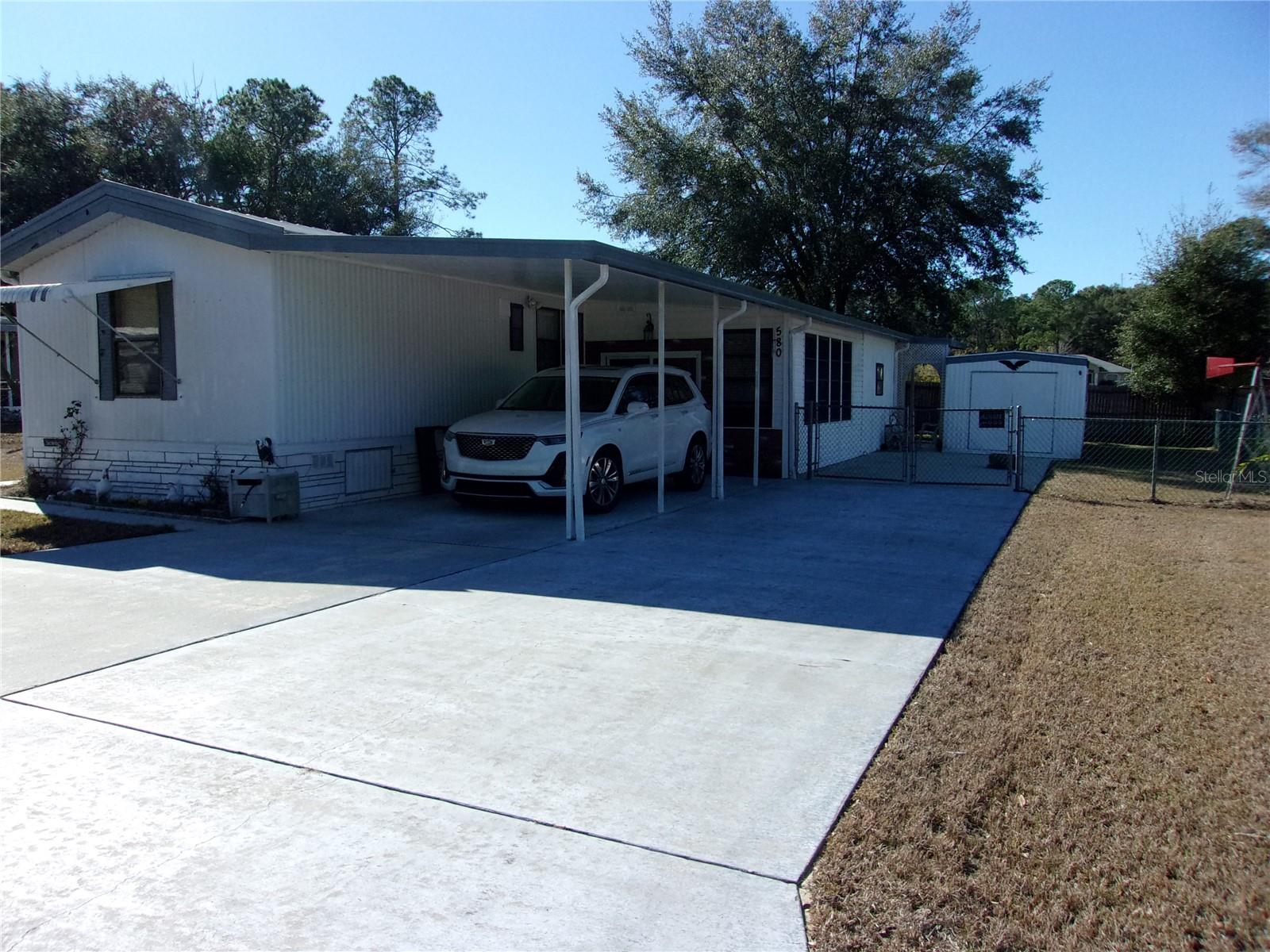 2 bedroom, 2 Bath mobile home for sale in all ages community of Ocala East Villas where you own your land as well. Pull up to the home and park under the carport or on the extra parking pad. Enter through the sliding glass doors to the Florida room with vinyl windows and to the impressive laundry room with countertops, a kitchen sink and an extra refrigerator-as well as the washer and dryer. Home boasts cathedral ceilings and split floor plan. Main bathroom has walk in shower and guest bath has tub/shower combo. secondary bedroom has a door to the outside allowing you to let your dog out into the fenced back yard without going all the way around the house. 10 x 20 outbuilding houses a great workshop and storage area with electricity connected. Stove is propane gas and home has tankless water heater that is on demand for just when you need hot water. Furnace is also propane. Come take a look and see what this home has to offer. Most of the furniture will stay with the home, so this would be great for you snowbirds looking for a great community where you own the land and the HOA fee is very affordable
