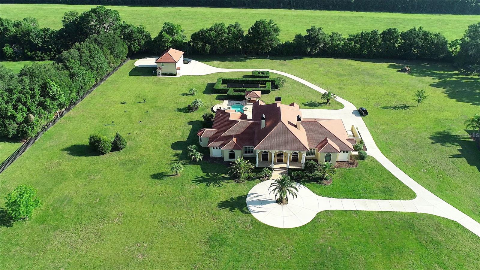 Set behind a private gate, on 6.8+/- acres, sits this stunning estate with style and elegance.
A large front patio presents itself as you walk up to 3 sets of stately front doors leading to the grand entry. Upon entering the main residence, you will be welcomed by an impressive entrance with soaring groin- vaulted ceilings and designer lighting. The entry hall is a central hub that seamlessly connects to spaces designed to welcome guests in lavish style. 3 En-suite bedrooms, 3 full and 2 partial baths with 8,295 SF living area. The 30 X 70 oversized display room with center fireplace, built-ins, and extensive recessed lighting in the ceiling to display your trophies, athletes, entertainers, and passionate hobbyists’ memorabilia. Adjoining room features lots of built-in for displaying other valuables. The family room and kitchen area open to the formal dining room and draw friends and family together into a social space that evokes inviting warmth, and an open layout that links with the gourmet kitchen, breakfast area, and outdoor spaces. The gourmet chef’s kitchen is outfitted with quality custom cabinetry, top-of-the-line appliances, center island, granite counter tops, two raised islands on each end for extra counter space and extra seating. The spacious executive office is complemented with solid African Padauk doors, cabinets, and coffered ceilings and generous sitting area. The bonus room is currently used as an additional office/copy room, but could be used for a multitude of purposes (exercise, hobby or craft room, etc.) Scullery area with cabinets, microwave, oven, dishwasher, large sink and pantry perfect for additional storage, workspace and prep area. The laundry room offers extra cabinets and laundry sink.
The primary bedroom exudes warmth and luxury with a luxurious bathroom, dual vanities, and a jetted tub overlooking the beautiful grounds. A swimming pool, Jacuzzi tub, plus an outdoor kitchen with built-in barbecue perfectly situated to enjoy the serene back resort style pool area.
Distinguished details include your private underground soundproof 50-foot range, concrete poured walls with R-55 wall factor barrier, all windows are double pane Pella doors and windows, barrel tile roof, crown molding and extensive lighting. Oversized 3 car garage with two side entry doors and half a bath. The upstairs guest house is 1581 SF and features 2-bedroom 2 bath, open kitchen-living.
The level of custom finishes throughout the estate setting this property apart from the competition.
