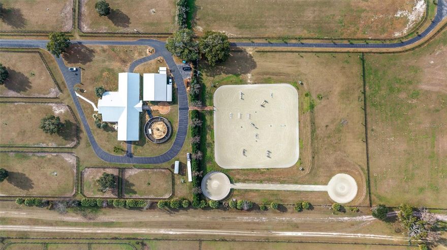 This fully built equestrian training and boarding facility is designed to support a professional program, offering the scale, layout, and infrastructure required for efficient daily operations. Located in Northwest Ocala’s highly sought-after Golden Corridor, this approximately 50-acre property is fully operational today while offering substantial room for expansion and long-term growth. The facility includes three barns totaling approximately 43 stalls, multiple on-site living quarters, and a complete training, conditioning, and recovery layout, thoughtfully designed to prioritize horse flow, labor efficiency, and functionality for serious operations. The main training barn features 14 oversized stalls with IDA rubber flooring throughout, insulated interior, updated electrical and lighting, new stall doors, industrial stall fans, and large ceiling-mounted HVLS fans for superior airflow and summer heat reduction, along with three cross-tie stations, a fly spray system, dedicated tack room, and laundry facilities. Attached to the main barn is an approximately 2,400 sq ft barn apartment with four private rooms, one bath, full kitchen, common area, designated office, storage, and direct barn access—ideal for on-site management or owner-operator living. Adjacent is a 40’ x 60’ open-sided conditioning and recovery barn featuring additional wash racks, a six-horse European-style walker with IDA rubber flooring, a shavings container with hydraulic roof lift, and space currently configured for therapy and spa use; equipment may be negotiated separately. Training amenities include a 200’ x 200’ LongWood riding arena, 150’ gymnastic pad, 60’ lunge circle, and 60’ round pen, all constructed with GGT footing and integrated sprinkler systems. The second barn is a ~4,700 sq ft center-aisle block barn with approximately 15 stalls and a new metal roof (2024), updated electrical and lighting, fly spray system, tack room with laundry and half bath, interior cross-ties with rubber flooring, and a covered double wash rack with hot water. The third barn is a wood-frame run-in barn with metal roof servicing the rear grazing pastures, allowing flexible turnout and shelter for additional horses. A 24’ x 50’ hay barn with new siding and additional storage sits adjacent to the second barn, serviced by a newly paved asphalt driveway. A brand-new 2025 three-bedroom, two-bath manufactured home provides additional on-site housing, along with climate-controlled storage in a heated and cooled Tough Shed and a 30’ x 50’ enclosed metal-roof structure currently used as an animal enclosure. The property is divided into 26 paddocks with automatic waterers and mature shade, including front turnouts with large shade trees, several paddocks with lean-to shelters and fans, and larger grazing areas to the rear. With established infrastructure, multiple living quarters, automatic water systems, and a prime Northwest Ocala location, this property offers exceptional efficiency and scalability for a professional equestrian operation while retaining the flexibility to evolve into a premier estate-level property over time