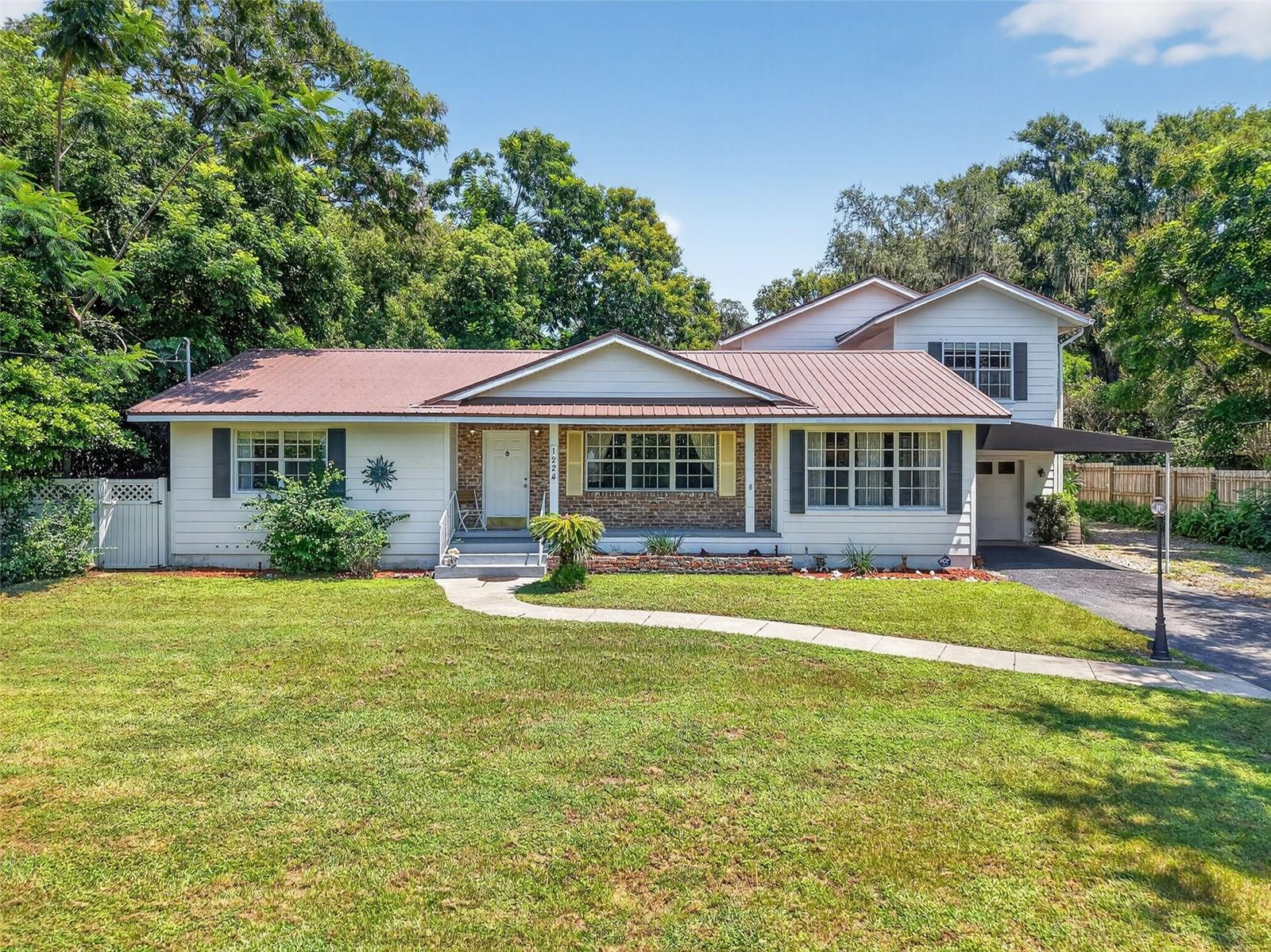 CHARMING 3/2 MOUNT DORA HOME WITH POOL, GARAGE, AND LARGE YARD. Here’s your opportunity to fulfill your dream of moving to historic Mount Dora to live in a home full of charm and character while not sacrificing practical amenities. Imagine spending a fun day downtown in one of the eclectic boutiques or the art gallery enjoying the many cafes, bakeries, or fine dining restaurants around town. Perhaps you have secured your boat at the full-service marina, and you invite friends to hop aboard and cruise through the famous Mount Dora canal to explore the popular Harris Chain of Lakes. At the end of a thrilling day, retreat home to your personal slice of Florida paradise. This beautiful and welcoming home is nestled onto a generous .41-acre parcel with just the right number of mature trees and foliage. The quintessential metal roof (2019) with gabled roofline and cozy front porch creates a ‘downhome’ feeling. Linger on the porch sipping iced tea while chatting with a neighbor. When you’re ready to come indoors you’ll find a bright and cheery interior rich in character and detail and infused with abundant natural light streaming in through large windows and doors. Thick crown molding and original hardwood floors speak to the original touches of quality craftmanship. The floor plan has great flow for entertaining. The spacious living room offers a decorative fireplace with a mantle for hanging holiday stockings and cards from loved ones. The adjoining dining room has unique, original built-ins and French doors to the rear pool deck. A cozy family room is connected to the living room with French doors that open wide to create even more sense of space. The family room evokes a feeling of rustic elegance with the rustic tile floors, tongue and groove wood-plank ceilings, and abundant wrap-around windows. What a great space to read a book or watch a movie. The galley kitchen has stainless appliances including a gas stove, and overlooks the pool and backyard. There’s also a Butler’s pantry for extra storage and a great coffee prep station. Built-ins abound here adding to the whimsey and charm! Two spacious bedrooms are downstairs, sharing a full bathroom with a shower. The staircase leads to the second story primary suite with tongue and groove ceiling, wood-laminate flooring, huge spaces for lounging, a walk-in closet, and an en-suite with dual sinks, a deep soaking tub, and a tiled shower. Florida life isn’t complete unless you have great outdoor spaces and this property does! Enjoy a covered carport and a 1-car garage, complete with a bonus living space, kitchenette, and full bathroom! Relax or entertain in the privacy fenced back yard with a paver patio, retractable sunshade awning, and a refreshing pool! The ample yard has loads of space for a fire-pit area or room for kids to run and play! What a wonderful home in a wonderful community!