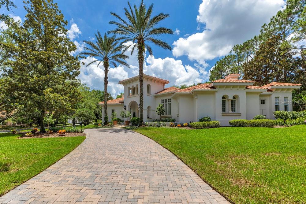A Masterpiece of Design in Isleworth – 6186 Louise Cove Drive. Stunning, design magazine-worthy residence nestled behind the exclusive 24-hour guard-gated community of Isleworth, one of Central Florida’s most prestigious neighborhoods. This exquisite estate sits on a spacious 0.75-acre corner lot, surrounded by mature landscaping and a stately circular driveway that sets the tone for the luxury that awaits inside. No expense was spared in the recent $1 million designer remodel, which brought in California-based interior designers to source the finest materials from around the globe. Step through grand arched solid wood double doors into a soaring foyer where 16-foot ceilings and imported white French oak floors flow throughout the home. Walls were meticulously finished to level 5 smoothness a testament to the craftsmanship and attention to detail throughout. Designed for both entertaining and everyday living, the open-concept family room centers around a venetian plaster fireplace and effortlessly flows into a show-stopping double island kitchen. Imported German cabinetry is complemented by one piece quartzite slabs and backsplash, while high-end appliances include a 6-burner Wolf range with double ovens, a paneled Thermador refrigerator & freezer, venetian plastered hood, beverage fridge, and under counter microwave are all seamlessly integrated for a refined look. Retreat to the expansive primary suite, where comfort meets luxury. Enjoy access to a private study, Florida room, and a spa-inspired bathroom featuring a stand-alone soaking tub, oversized glass shower with handmade 4x4 Moroccan tile, French brass fixtures, and custom lighting. Primary suite also features a spacious walk-in closet offering custom built-ins, providing both elegance and functionality. The home’s Santorini-inspired full pool bath is a work of art in itself, with artisan stucco finishes adorning every surface. Each secondary bedroom is an en-suite, with marble or handcrafted tile finishes and ample closet space. Outdoors, your private fenced backyard oasis features a heated pool & spa, covered summer kitchen, and expansive lanai, perfect for enjoying Florida’s year-round sunshine. Additional highlights include a whole-house generator, tankless water heaters, four AC units, and a designer laundry room with imported German cabinetry. Live minutes from world-class attractions, dining, and elite schools, yet enjoy the serenity and security of one of the region’s most sought-after enclaves.