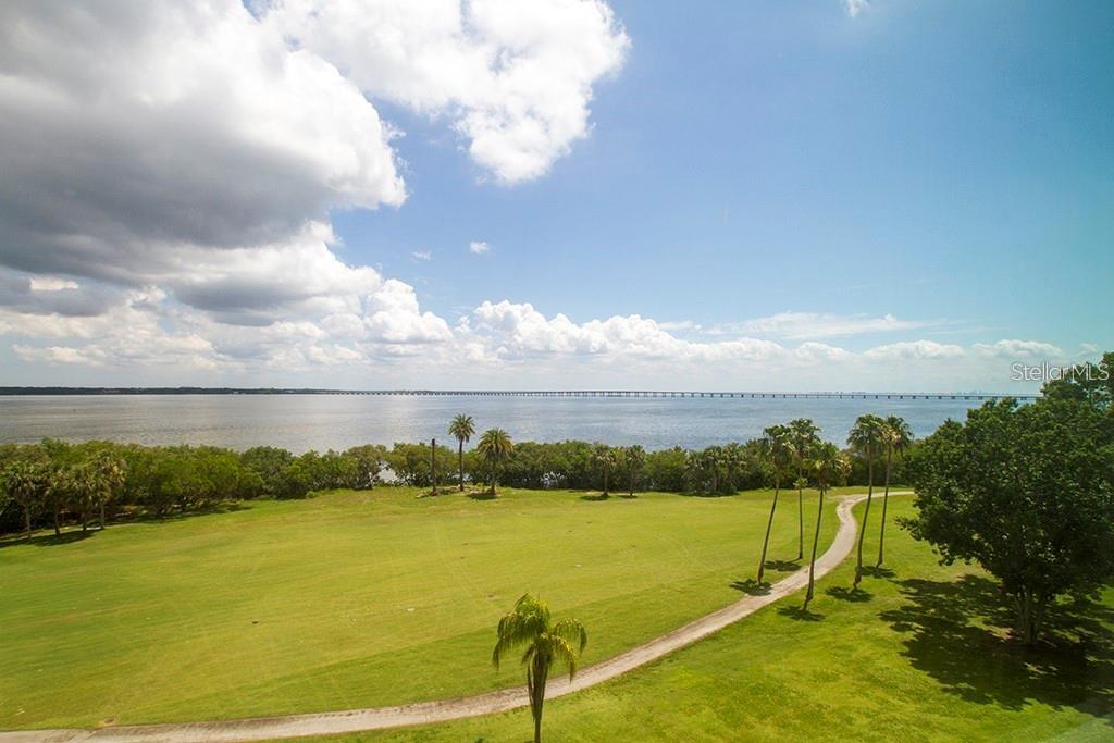 Breathtaking panoramic views of Tampa Bay and the lush fairways of Cove Cay Golf Course set the stage for this 7th-floor 2-bedroom, 2-bath condo. Inside, the open kitchen is a true standout—renovated with raised panel white cabinetry, striking granite countertops, a spacious serving/snack bar, undermount stainless sink, and a full suite of stainless steel appliances, including a built-in French door refrigerator. The raised ceiling, complete with crown moulding and center fan, adds to the custom feel.
The open living area is designed to highlight the stunning view, with brand-new carpet, custom built-in shelving, and sliding glass doors leading to the screened-in porch—the perfect spot to unwind. The spacious primary bedroom also shares the incredible view and offers an en suite bath with vanity space, a walk-in closet, and a separate shower. The second bedroom features a high-set window for natural light and privacy, making it ideal for guests or a home office.
This unit also includes exclusive access to a private laundry room just across the hall, complete with washer, dryer, and plenty of storage. A covered carport rounds out this impressive package. Lush landscaping throughout the complex is always pleasant. Welcome to resort-style living at its best in the gated, waterfront community of Cove Cay!