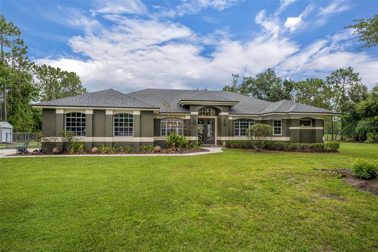 EQUESTRIAN OASIS IN THE HEART OF OVIEDO…Nestled beyond a gated entrance on a quiet private road, this breathtaking equestrian estate offers the perfect blend of luxury, privacy, and rural charm—yet remains just minutes from shopping, dining, and commuter routes. Set on over five acres of usable land, this custom-built home showcases soaring ceilings, expansive open living spaces, and a layout designed for both entertaining and everyday living. The gracious primary suite is a true retreat, featuring elegant tray ceilings and three walk-in closets with striking barn-style doors. The spa-inspired en-suite bath is a showstopper, with a jetted soaking tub set against a waterfall backdrop, an oversized walk-in shower for two with separate his and her drying areas, a private water closet, and a lighted makeup mirror inspired by the luxury suites at The Equestrian Hotel. An on-demand hot water system adds convenience and comfort. The spacious great room opens through disappearing sliding glass doors to a covered lanai with a resort style PebbleTec heated pool and spa, ideal for seamless indoor-outdoor living. The kitchen offers a breakfast bar, café-style dining nook, and connects to a formal dining room that easily accommodates eight guests for special gatherings.
Equestrian features include a center-aisle barn with five 12x12 matted stalls, each equipped with tongue-and-groove wood fronts, sliding stall doors, and automatic waterers. The barn includes a Shoo-Fly insect control system, a hot water wash area, an air-conditioned tack room, and an additional climate-controlled feed and medication supply room for convenience and safety. After a ride in your grass arena, enjoy the serene beauty of the surrounding land or take a peaceful trail ride in the 250-acre Econ Wilderness Area—located just across the road from your property. There’s also a spacious, fully fenced yard, perfect for your four-legged family members to safely roam and play. This rare property is zoned for highly rated schools, including sought-after Hagerty High School. Located near 434, 419, Lockwood Boulevard, and McCulloch Road, this estate offers both tranquility and accessibility. This is more than a home, it’s a lifestyle. Call today to schedule your private showing of this exceptional equestrian retreat in the heart of Oviedo!