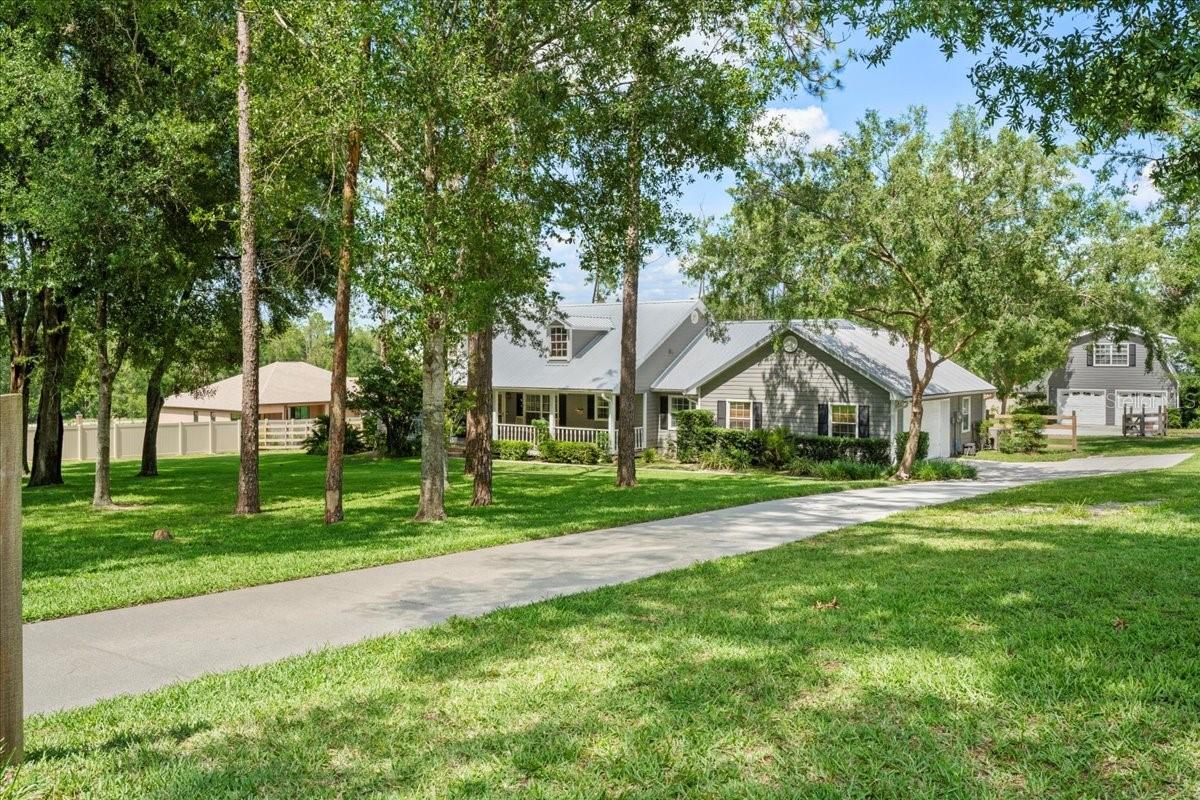 Discover the perfect blend of quality, comfort, and privacy in this beautifully crafted custom home by Pete Richter Construction. Nestled on 1.33 wooded acres along a quiet paved road, this 3-bedroom, 2-bathroom pool home with two garages offers peace, energy efficiency, and generous space both inside and out, with no HOA. Built to stand the test of time, the home features poly-steel construction, 9¼" Styrofoam blocks filled with concrete and rebar, offering exceptional insulation and durability. A newer metal roof (only 3 years old) and a hardwired alarm system with motion sensors on all doors and windows provide added security and peace of mind. The Ring camera system, fully transferable at closing, enhances this layer of smart protection. Inside, a spacious split floor plan welcomes you with volume ceilings, laminate flooring throughout, and ceramic tile in all wet areas. The kitchen, outfitted with recently updated stainless steel appliances, flows effortlessly into a large living area with a cozy fireplace, perfect for entertaining or quiet family evenings. The oversized primary suite includes dual walk-in closets, a garden tub, and a separate shower for your comfort and convenience. Enjoy the best of Florida living year-round with a newly updated screened-in inground pool, complete with a brand-new cage and covered patio, ideal for outdoor gatherings or relaxing in the sun. A large front porch adds charm and offers the perfect spot to take in peaceful sunset views. This home goes beyond expectations with an attached 2-car garage, plus a detached, air-conditioned 2-car garage featuring a spacious upstairs office or workshop, offering a total of four garage spaces for unmatched flexibility. Smart features abound, including a WiFi-capable irrigation system, garage access, and side entry pedestrian door control via phone. Natural gas is also available for added convenience and accessibility. Surrounded by mature trees and natural landscaping, this move-in-ready home delivers the best of country living with modern features and energy-efficient design. Located just minutes from shopping conveniences such as Publix, Walmart, Rural King, Lowe’s, and others. Don’t miss this rare opportunity to own a truly unique and exceptionally well-built home. Schedule your private showing today, your dream home awaits!