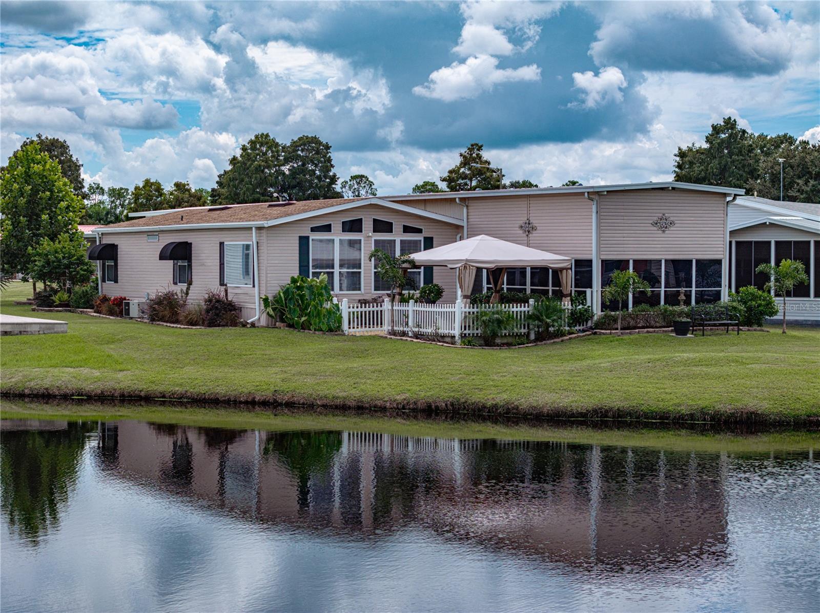 Welcome home to this meticulously updated and thoughtfully enhanced waterfront residence in the highly sought-after community of Mount Olive Shores. This immaculate home offers a perfect blend of modern luxury and timeless elegance, boasting numerous upgrades that elevate its appeal. As you step inside, you will be greeted by the warmth of new luxury engineered wood flooring (2023), seamlessly flowing throughout the living spaces, creating a cozy and inviting atmosphere. The kitchen, a culinary haven, features top-of-the-line stainless steel appliances and a stylish backsplash that adds a touch of sophistication to the space. Natural light bathes the interior thanks to two new designer glass doors that amplify the sense of openness and provide stunning views of the surrounding landscape and water. Every detail has been carefully considered, from the all-new wood blinds that add privacy and style to the custom window awnings that enhance the home's curb appeal. The newly installed roof (2023), patio (2023), and landscaping (2023) all contribute to the property's freshness and curb appeal. Outside, the newly laid cement patio provides an ideal spot for entertaining or enjoying quiet moments by the water. The upgraded RV power to 50-amp service (2022) and recently extended RV port open possibilities for travel enthusiasts. The home's interior and exterior have been given a fresh coat of paint, creating a clean and modern aesthetic. Additionally, new ceiling fans enhance airflow and add a touch of contemporary design to each room. Practical updates, such as new tie-down straps (2022), ensure the home's structural integrity. The attention to detail and commitment to quality craftsmanship are evident throughout this property, making it a true turnkey and move-in-ready residence. A One-Year Home Warranty will be included with the purchase. Discover a lifestyle of comfort, style, and modern convenience at your private oasis. This is more than a home; it's an invitation to indulge in the finest features and luxuries Mount Olive Shores offers. This community is just minutes from I-4 and gives you quick access to local theme parks and attractions, retail, medical facilities, major metro areas, and local beaches. Mount Olive Shores is a Class A Motor Home, Deed Restricted Community. You must own or lease a Class A Motor Home the first year of accumulated residency. The annual HOA fee includes lawn maintenance. Don't miss the opportunity to make this exquisite property your own!