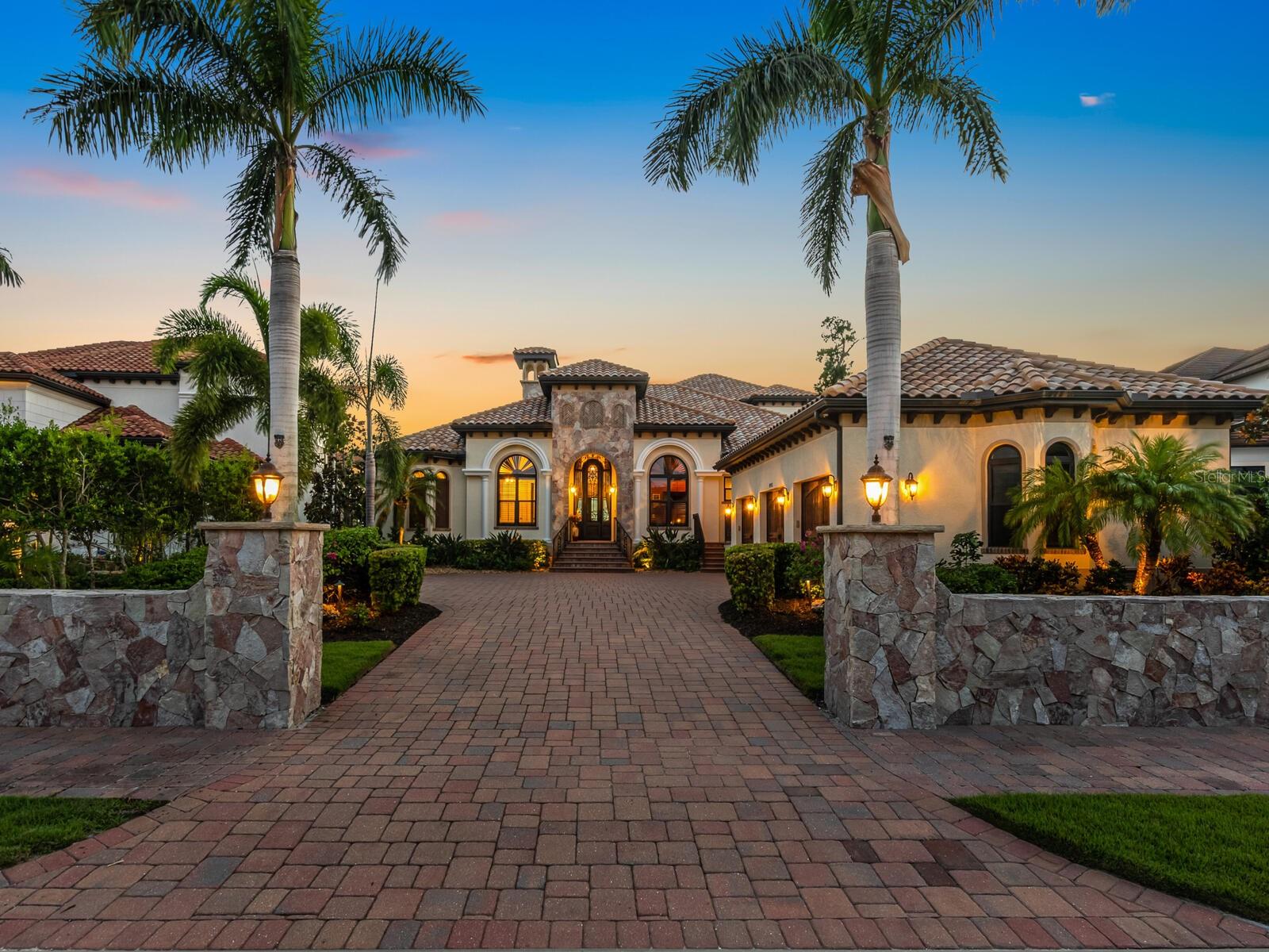 Welcome to the market for the first time, this elegant custom built estate located in the exclusive private gated community of Blackburn Ridge, situated on Blackburn Bay and the Intracoastal Waterway which is near the communities of Osprey, Laurel, Nokomis, and Casey Key.
Welcoming you at the entry to this estate, you will find a 68’ stone wall, which each piece was hand cut to give a dry fit appearance. Enter through the hand crafted custom entryway door and immediately take in the view from the beautiful water beyond. This estate boasts 4 full bedrooms and 5 full baths, with the entire second story designed for entertainment with its theater room seating and built in bar, complete with dishwasher, ice maker and wine cooler. There is also a full bath and murphy bed, which this space could easily serve as a second master suite is so desired. From the second floor, you can enjoy the natural beauty of the water views from the full-length balcony. The chef’s kitchen will delight all cooking professionals and enthusiasts with its expansive island and Thermador appliances. The custom wine cellar with its vineyard murals will make you think you are in Tuscany! Host your guests in the stunning dining room as you enjoy watching the sunset. The living room creates a fabulous gathering space with its custom fireplace and volume ceilings. The immense master suite provides waterfront views, separate sitting area, and his and hers custom walk-in closets. The master bath includes soaking tub, oversized shower, and private commode. Jack and Jill bedrooms are ensuite, as well as the remaining bedroom. Make endless memories with family and friends while entertaining on the patio, with full kitchen and saltwater pool. The 90’ no profile dock with hydraulic remote-control lift allows you access to the intracoastal waterway via kayak or paddle board. If you are a boater, there is a full-service Marina just minutes away. To complete this estate is an oversized 3 car garage, with elevated ceilings for all your storage needs, whole house generator, impact windows and doors, 2 a/c’s with dehumidifiers, water and electric at dock, solar outdoor lighting, fenced in dog run, and mini split in wine cellar. Just a short drive to the top Gulf beaches, shopping, and restaurants, this is the perfect place to live the luxurious waterfront lifestyle that the West Coast of Florida has to offer.
