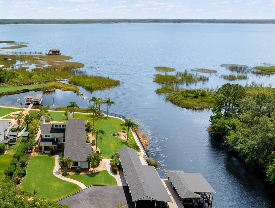 RARE OPPORTUNITY!  This unique property is more than just a home. It’s a lifestyle. Over 450 ft WATER FRONTAGE and NO HOA on Lake Hart!   This picturesque CORNER waterfront home is a dream come true for the boating and water enthusiasts.  Nestled in a serene location at the end of a quiet, tree-lined street, this secluded 1.15 AC property is truly special.  The combination of lake and canal views, along with the unique corner location, provides privacy as well as a sense of expansive openness.  Experience breathtaking sunrises and shimmering moon glades from your eastward facing backyard.  One of the most distinctive features of this waterfront property is the grandfathered in PRIVATE boat ramp. Also attached to the property is a covered boat dock equipped with 3 boat lifts.  Those who enjoy the outdoors will appreciate the backyard oasis with the gentle breeze and the sound of water trickling from a rock waterfall into a sparkling pool and spa.  Prepare and serve amazing outdoor meals from your outdoor lanai kitchen. 
Step inside to find a stunning 4 bedroom 3 bathroom home that has been meticulously updated into a beautiful coastal design bathed in natural light.  An open and airy great room with inviting 19 ft stone fireplace, wood beamed vaulted ceiling, patio doors and scenic view of Lake Hart and Moss Park area greet you. The light coastal design is carried through every room with new Pella windows, new paint and LVP flooring throughout. Open sitting space with large picture window blend seamlessly into dining area with built in buffet. Attention to detail in the kitchen with new subway tile, quartz countertops, new cabinets and appliances, garden window, and built in window seating area. Enjoy a shiplap paneling laundry area, built in mudroom storage drop zone, leading into an oversize family/media room finished with Wainscot Paneling great for large gatherings or movie nights. There are two comfortable bedrooms and a full bathroom with walk-in shower on the main level. As you make your way upstairs, a loft bridge overlooks the Great room. To the left is a bedroom, with ensuite bathroom and walk-in closet. The well-appointed primary suite transports you to a tranquil oasis with an unobstructed water view through the massive 12 ft by 6 ft window and surrounding wall of windows. The primary bathroom with dual sinks, separate tiled shower, soaking tub and walk-in closet completes your personal oasis. The hobbyist and gardener will love the climate tempered workroom space brightly lit with plenty of storage space and a separate insulated cold storage room. Attached is an oversized 3 car carport and plenty of space for extra parking. Interested in living off the grid? The detached shed/carport roof offers perfect space for future installation of a large solar panel array. This property is zoned A-2 allowing for many types of animals including chickens as well as allowing many types of vegetables and flowers. The home has deep well water, a whole home water filtration system and lawn irrigation source is fed by lake water. As dusk falls, the manicured yard, sidewalks and palm trees come alive with landscape pathway lighting and up lighting throughout the property.  This private sanctuary is ideally situated in the highly sought-after Lake Nona area, only 15 min to Orlando International Airport, less than 30 min to area theme parks and Downtown Orlando.