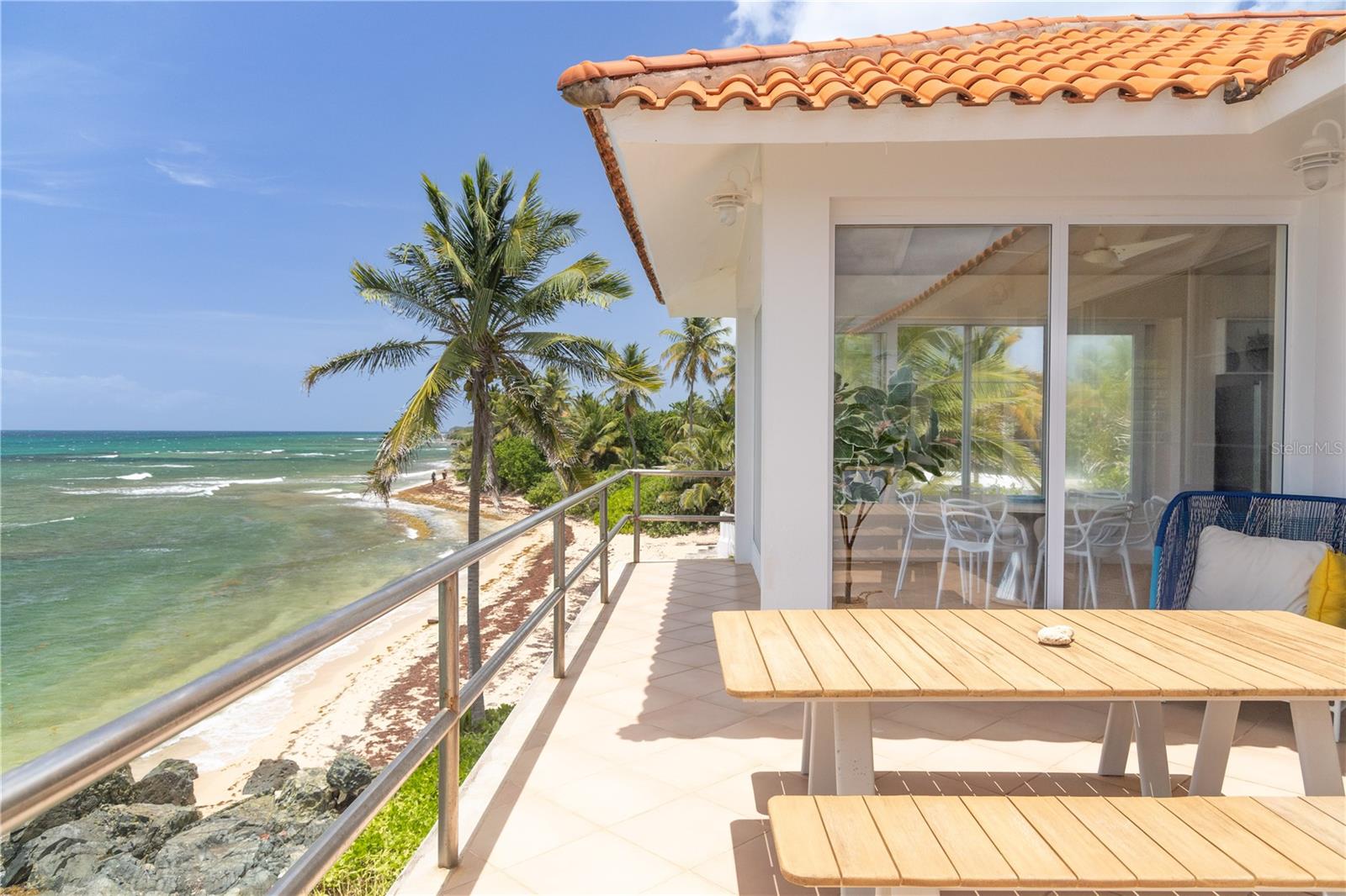 Las Piedras is a rare oceanfront property offering unmatched views and a remarkable connection to its surroundings. Set just above the clear waters of Vieques’ north shore, the home captures a full 180-degree view of the Caribbean—stretching from the coral-lined shallows below to the distant outlines of Culebra, St. Thomas, and St. John on the horizon. To the west, the mountains of mainland Puerto Rico rise against the sky, anchoring the landscape in every direction.
A private driveway lined with mature palms and dense tropical foliage leads to the home’s entrance, which reveals a contemporary structure with subtle Spanish Colonial elements—most notably its terracotta-tiled, hipped roof. The three-story residence is solidly built and thoughtfully laid out, with four bedrooms, two and a half baths, and multiple indoor-outdoor living areas that make the most of the setting.
The upper level is the heart of the home, with vaulted ceilings and an open-concept kitchen, dining, and living area. Floor-to-ceiling windows and doors frame uninterrupted views of the ocean from nearly every angle. The living space opens onto a wide ocean-facing balcony, ideal for sun lounging or outdoor dining. A half bath and an adjacent auxiliary room—currently outfitted with a bed—offer potential for a flexible use space or an additional bathroom conversion.
Anchoring the structure is a central staircase built directly into the landscape, incorporating large natural boulders that not only define the aesthetic but also act as part of the home’s foundation. The second level houses the primary sleeping quarters, including two ocean-view bedrooms. The principal suite includes a modern ensuite bath with a polished cement shower and integrated sink. This level also features a smaller sitting room with a hidden Murphy bed, which opens onto a balcony overlooking the sea and connecting to the pool terrace. A spacious second full bath includes an oversized built-in tiled tub.
The ground floor offers two additional cozy, well-proportioned bedrooms and a common area with a reading nook. There’s also a modern full bathroom with a polished cement shower and built-in sink, positioned next to a large laundry and storage room. Beneath the pool deck is a utility and pump room, discreetly tucked away from the main living areas. The bedrooms are fully air-conditioned for comfort, while the rest of the home is designed to take full advantage of natural ventilation, ocean breezes, and crosswinds.
Las Piedras combines privacy and presence—set apart from the street, with direct access to the quiet sands of La Chata beach. Landscaped with native palms and low-maintenance gardens, the property includes a walking path that circles the house and offers seamless access to every corner of this uniquely situated coastal home. A gated entrance opens to a parking area that comfortably accommodates two vehicles.
Whether as a personal retreat, an elegant space for entertaining, or an income-producing asset, Las Piedras delivers. It is currently operated as a highly successful luxury vacation rental, offering immediate investment potential with a proven rental history.