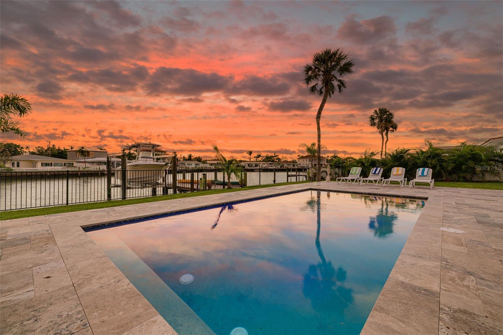 Welcome to coastal living at its finest in the sought-after Palm Point neighborhood of St. Pete Beach! Perfectly situated within walking distance to the vibrant Corey Avenue Sunday Market, the sugar-sand beaches of the Gulf, and a host of popular restaurants, shops, and bars, this beautifully renovated home blends luxury, style, and functionality. Set on 75 feet of waterfront along a wide canal of Boca Ciega Bay, this property is a boater’s dream—complete with a (2024) polywood dock equipped with both electric and water supply, a (2024) 10,000 lb boat lift with Gem remote, and access to the open water. The newly built 2024 custom pool features aqua blue Stonescape mini pebble finish, heater and chiller, and is surrounded by a travertine deck that transforms the backyard into a private tropical retreat. Inside, no detail has been overlooked. A spacious open-concept layout greets you with travertine flooring throughout, drawing your eye from the front door straight through to your waterfront oasis. The stylish kitchen overlooks the living and dining areas, boasting leathered granite countertops, abundant cabinetry, and brand-new appliances. The living room features a stunning brick accent wall with mid-century modern sconces, while the statement chandelier above the dining table adds dramatic flair. The Florida room is drenched in natural light with a wall of windows overlooking the sparkling pool and water beyond. A split bedroom layout ensures privacy, with the primary suite offering water views, a walk-in closet, and a luxurious ensuite bath. Both bathrooms are fully updated (2024) with Carrara Italian marble shower stalls, lighted mirrors, and new vanities. The spacious front guest bedroom includes an oversized closet, and the rear guest bedroom also enjoys serene pool and water views. Additional features include: fresh interior and exterior paint ~ new doors and modern lighting throughout ~ professionally landscaped with privacy fencing ~ reclaimed water irrigation system ~ 1-car garage with laundry hook-up for stackable front-load washer/dryer ~ (2024) HVAC with all new ductwork ~ (2024) water heater ~ (2024) whole house water filtration systemw ith water softener ~ (2024) electrical panel. Whether you're looking for a full-time residence or a beachside retreat, this turn-key waterfront gem checks every box. Experience the best of St. Pete Beach living—schedule your private showing today!