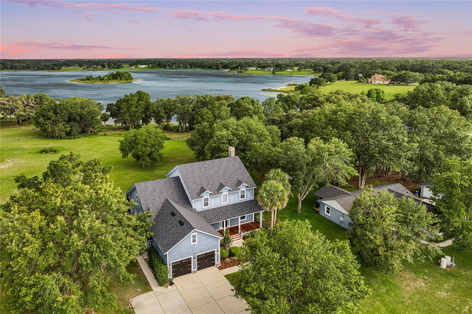 The owners approved lender will give the buyer up to $5,000 in closing costs assistance on the purchase of this home. Welcome to this extraordinary custom-built farmhouse-style estate — a rare offering that seamlessly blends timeless elegance with pastoral serenity. Encompassing over 4,000 square feet, the main residence is set amidst six acres of lush, fenced pastures and sweeping lakefront views, offering the perfect setting for those seeking a peaceful retreat with multigenerational flexibility.
One of the most exceptional features of this property is the beautifully crafted two-bedroom, two-bath guest cottage, thoughtfully positioned on the grounds for privacy and comfort — ideal for extended family, guests, or even rental income.
An entry and a long, driveway lead to the main residence, a picture-perfect two-story farmhouse wrapped in stone accents and painted in soothing blue hues. A wide, rocking-chair front porch and dormer windows complete the idyllic setting.
Step inside to warm wood flooring, an elegant home office, and a formal dining room adorned with crown molding and faux blinds dress the window. The chef’s kitchen is the heart of the home, outfitted with rich maple cabinetry with glass fronts, Silestone countertops, staggered tile backsplash, and professional-grade appliances including a six-burner gas range, dual ovens, and a warming drawer. A generous walk-in pantry and adjacent eat-in kitchen—framed by panoramic windows overlooking green pastures—create a warm and inviting space for everyday living.
The family room features hardwood floors, a cozy fireplace, and French doors that open to mesmerizing views of the tranquil lake.
This home offers a rare and sought-after feature — dual owner’s suites, one on the main level and one upstairs, perfect for multigenerational living or hosting long-term guests in ultimate comfort. The primary suite on the first floor is a private sanctuary, complete with lake views, direct balcony access, crown molding, and a walk-in closet by California Closets. The en suite bath features white cabinetry, desert-brown granite counters, a soaking tub surrounded by crisp white wainscoting, and a spacious walk-in shower with custom marble finishes.
Upstairs, you’ll find the second owner's suite, well-appointed, along with additional secondary bedrooms, ample storage, and a bonus/ theater room, prewired for surround sound and finished with plush carpeting for the ultimate entertainment experience.
Out back, a large, screened patio provides the perfect spot for relaxing or hosting weekend barbecues. Follow the gently sloping landscape to your private boathouse, ready to accommodate a 24'+ vessel — perfect for enjoying endless days on the water.
The guest cottage, has its own address encompassing over 1,200 sq. ft. — offers a full kitchen, charming living spaces, two bedrooms, two baths with walk in showers and the same scenic lake and pasture views, making it ideal for loved ones or long-term visitors. Bring your horses, boats, toys, and dreams — this is more than just a home; it's a lifestyle. A truly unique country estate where comfort, charm, and natural beauty live in perfect harmony.
