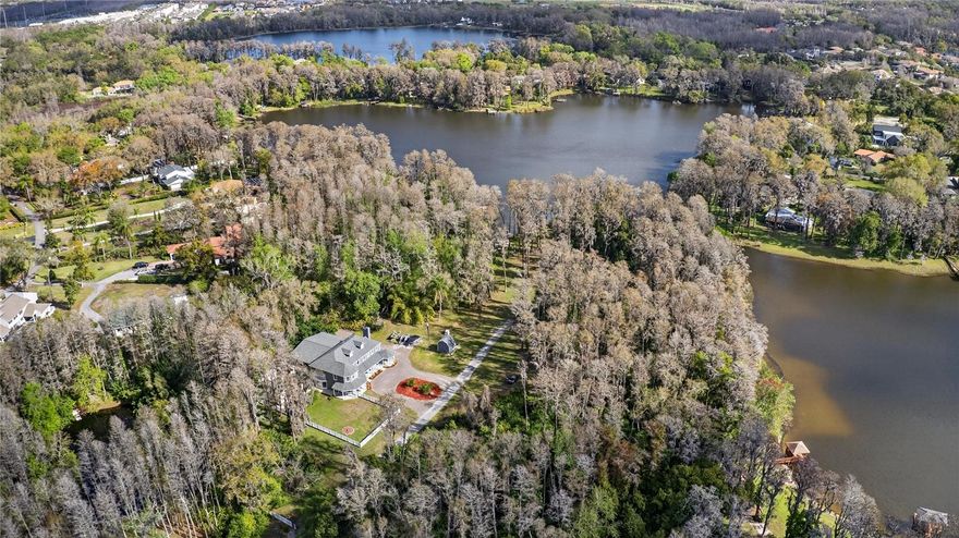 Tucked beyond a private GATED drive beneath a canopy of towering oaks, this LAKESIDE estate spans 2.8 acres (Fall 2025 survey) of pristine ski-lake frontage, offering a rare blend of privacy, acreage, and waterfront living. Set well back from the road, the 4,071 sq ft residence features 5 bedrooms, 3 full baths, 2 half baths, and a 3-car garage, surrounded by sweeping lawns, mature trees, and tranquil water views. A circular drive introduces the stately Southern-inspired façade, highlighted by an expansive wraparound porch and distinctive pavilion-style turret—an architectural presence designed for both elegance and comfort. Inside, soaring ceilings and oversized windows fill the open-concept layout with natural light. Porcelain tile flooring flows throughout the main living areas, complemented by crown molding and refined architectural detailing. The dramatic family room is anchored by a sleek fireplace feature wall and a remarkable 350-gallon built-in aquarium, creating an unforgettable focal point. Floor-to-ceiling windows frame panoramic backyard views. The home was completely remodeled in 2020. Overlooking the two-story family room with 25’ ceilings and balcony above, the chef’s kitchen is striking and functional. Crisp custom cabinetry pairs beautifully with onyx countertops and an oversized island with seating—ideal for gatherings large or small. Stainless steel appliances, designer tile backsplash, and abundant storage complete the space. Just off the kitchen, a designer half bath showcases Brazilian blue quartzite countertops, adding a bold and sophisticated touch. Three additional bedrooms and a well-appointed laundry room are conveniently located on the main level. Upstairs, the private primary suite offers exceptional space and balcony access overlooking the backyard. A custom walk-in closet with built-in organization provides both function and style. Sliding barn doors lead to the spa-inspired bath, where separate Brazilian blue quartzite vanities are complemented by high-end fixtures, designer lighting, and refined finishes throughout. Relax in the soaking tub with built-in television or enjoy the expansive glass-enclosed shower, thoughtfully designed to create a true retreat experience. A versatile upstairs bonus room provides flexible space for a home office, fitness studio, media room, or play space. Outdoor living is equally impressive. A newly paved pool deck surrounds the freeform pool, creating expansive entertaining areas framed by a charming picket fence. A covered pavilion with built-in bar, mounted television, and convenient half bath makes hosting effortless year-round. A winding backyard path leads to 32-acre Saddleback Lake, where jet skiing, boating, fishing, and peaceful sunset views await. With nearly three acres of usable land and multiple water features, this property delivers an exceptional lakefront lifestyle. Under recent appraised value! Zoned for highly regarded Schwarzkopf Elementary, Martinez Middle, and Steinbrenner High School. Significant upgrades include new roof 2022, 3 A/C units 2020, exterior paint 2025, and an energy-efficient pool pump 2025. Additional 2020 improvements include a tankless water heater, 3 impact-rated sliding glass doors, and a Culligan whole-home water filtration system. The property also offers a security system with cameras and a storage shed. Experience the privacy, space, and waterfront lifestyle this extraordinary estate offers—schedule your private showing today.