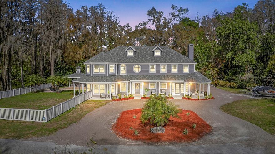 Tucked beyond a private GATED drive beneath a canopy of towering oaks, this LAKESIDE estate spans 2.8 acres (Fall 2025 survey) of pristine ski-lake frontage, offering a rare blend of privacy, acreage, and waterfront living. Set well back from the road, the 4,071 sq ft residence features 5 bedrooms, 3 full baths, 2 half baths, and a 3-car garage, surrounded by sweeping lawns, mature trees, and tranquil water views. A circular drive introduces the stately Southern-inspired façade, highlighted by an expansive wraparound porch and distinctive pavilion-style turret—an architectural presence designed for both elegance and comfort. Inside, soaring ceilings and oversized windows fill the open-concept layout with natural light. Porcelain tile flooring flows throughout the main living areas, complemented by crown molding and refined architectural detailing. The dramatic family room is anchored by a sleek fireplace feature wall and a remarkable 350-gallon built-in aquarium, creating an unforgettable focal point. Floor-to-ceiling windows frame panoramic backyard views. The home was completely remodeled in 2020. Overlooking the two-story family room with 25’ ceilings and balcony above, the chef’s kitchen is striking and functional. Crisp custom cabinetry pairs beautifully with onyx countertops and an oversized island with seating—ideal for gatherings large or small. Stainless steel appliances, designer tile backsplash, and abundant storage complete the space. Just off the kitchen, a designer half bath showcases Brazilian blue quartzite countertops, adding a bold and sophisticated touch. Three additional bedrooms and a well-appointed laundry room are conveniently located on the main level. Upstairs, the private primary suite offers exceptional space and balcony access overlooking the backyard. A custom walk-in closet with built-in organization provides both function and style. Sliding barn doors lead to the spa-inspired bath, where separate Brazilian blue quartzite vanities are complemented by high-end fixtures, designer lighting, and refined finishes throughout. Relax in the soaking tub with built-in television or enjoy the expansive glass-enclosed shower, thoughtfully designed to create a true retreat experience. A versatile upstairs bonus room provides flexible space for a home office, fitness studio, media room, or play space. Outdoor living is equally impressive. A newly paved pool deck surrounds the freeform pool, creating expansive entertaining areas framed by a charming picket fence. A covered pavilion with built-in bar, mounted television, and convenient half bath makes hosting effortless year-round. A winding backyard path leads to 32-acre Saddleback Lake, where jet skiing, boating, fishing, and peaceful sunset views await. With nearly three acres of usable land and multiple water features, this property delivers an exceptional lakefront lifestyle. Under recent appraised value! Zoned for highly regarded Schwarzkopf Elementary, Martinez Middle, and Steinbrenner High School. Significant upgrades include new roof 2022, 3 A/C units 2020, exterior paint 2025, and an energy-efficient pool pump 2025. Additional 2020 improvements include a tankless water heater, 3 impact-rated sliding glass doors, and a Culligan whole-home water filtration system. The property also offers a security system with cameras and a storage shed. Experience the privacy, space, and waterfront lifestyle this extraordinary estate offers—schedule your private showing today.