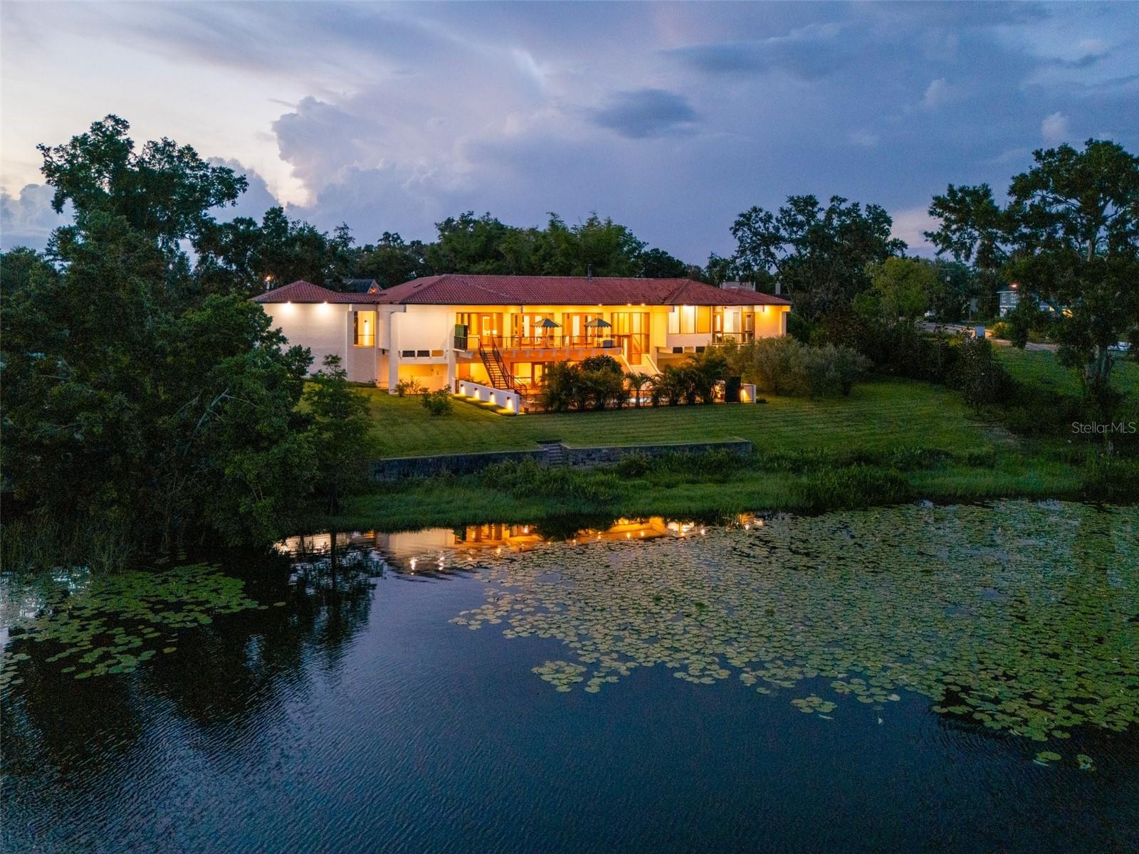 There was a time when homes were designed to last—and this is one of them. Designed by award-winning architect Gene Leedy, this south-facing lakefront residence embodies a legacy of modernism uniquely attuned to Florida’s landscape and climate. As a founding voice of the Sarasota School of Architecture, Leedy’s vision was ahead of its time, helping to shape a movement that left its mark on architecture around the world. Designed in 2006 for his daughter, this residence reflects decades of innovation—every detail considered, nothing spared. Step inside and you enter the mind of a true visionary—where nothing was done without purpose, and every detail was designed for modern living. From the soaring 15-foot ceilings to the graceful grain of custom woodwork, from ample storage to quietly integrated modern comforts, every detail speaks to Leedy’s belief that beauty and function must coexist. Leedy’s design masterfully merges indoors and out drawing Florida’s natural beauty into the flow of daily life with floor-to-ceiling windows and abundant outdoor living—more than 5,700 square feet—allow light, sky, and greenery to infuse each space. Courtyards and balconies offer a sense of retreat from every main room and bedroom. Built with Gene Leedy’s signature cantilevered style, the home is elevated by pre-stressed concrete beams, allowing it to float gracefully above Lake Otis—high and dry. Inside, custom cabinetry is found throughout made of beechwood, with doors, trim, and built-ins crafted with warmth and intention. The kitchen strikes a perfect balance of form and function, anchored by a VIKING gas range, Sub-Zero refrigerator, dual dishwashers, granite countertops, and a wine fridge—designed for easy everyday living and entertaining. Engineered for resilience, the home includes hurricane-rated tempered windows and doors, underground power lines, a full-home generator, surge protection, dual HVAC zones, imported Venezuelan clay roof tiles, a 4-foot concrete wall around the pool and modern fiber-optic connectivity— without compromising its architectural integrity. Including two separate garages with a total of four parking spaces with plenty of room for an RV or boat. Upstairs, soft natural light and gas/wood-burning fireplaces create space for stillness. Though the interior spans over 5,100 square feet, it feels remarkably cozy and serene. Downstairs, a generous pool room with wet bar opens directly to the pool deck and lakefront—made for open-air entertaining, dining and quiet nights on the lake. The resurfaced lap pool and spa, heated by natural gas, are surrounded by lush landscaping and lighting, including Magnolia trees and Sicilian olive trees that sway just outside the primary suite. The shoreline invites native birds and wildlife, while offering front-row seats to holiday fireworks and golden sunsets. There is ample room to add a dock and boathouse—perfect for afternoons on the water, boating, or waterskiing.For those who appreciate timeless design and refined craftsmanship, this is a rare opportunity to be part of an architectural legacy. Schedule your showing today.