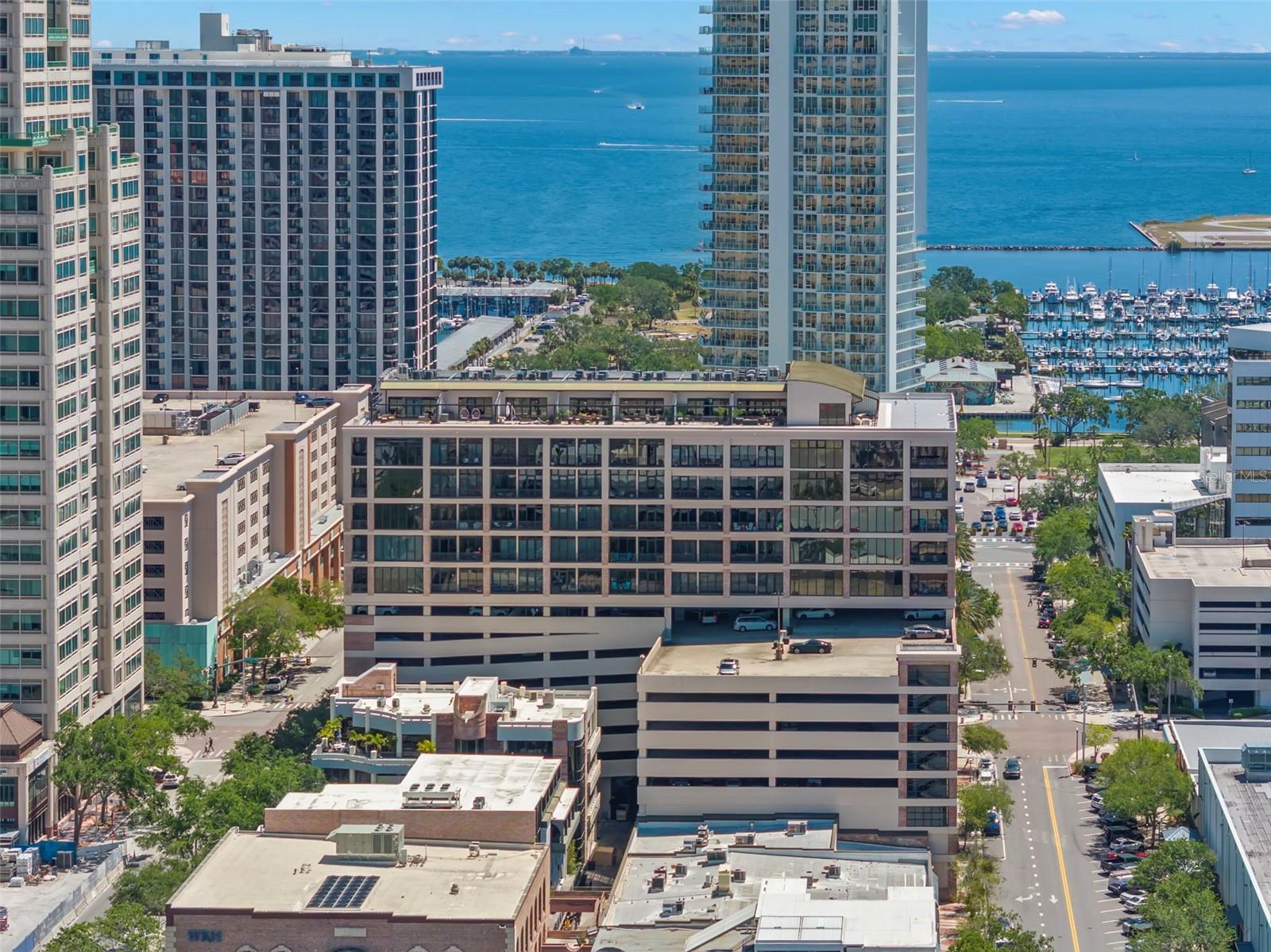 One or more photo(s) has been virtually staged. Modern industrial elegance awaits in this stunning one-bedroom, one-bath residence in the highly sought-after McNulty Lofts, located in vibrant downtown St. Petersburg. From the moment you enter, you're greeted by breathtaking views of sparkling Tampa Bay, perfectly framed by the city’s dazzling skyline, beautiful day and night, and a wall of floor-to-ceiling windows that flood the space with natural light. This industrial-style loft seamlessly blends contemporary design with timeless character. Ceilings soaring over 11', exposed spiral ductwork, and a brick accent wall bring authentic charm, while an open-concept floor plan offers modern comfort and versatility. The well-designed kitchen offers granite countertops, rich wood cabinetry, stainless steel appliances, and a spacious center island, ideal for cooking and entertaining. The spacious bedroom includes a walk-in closet, easy access to the laundry room, and private access to the bathroom. Enjoy unmatched convenience with resort-style amenities including secured entry, stylish reception area with lounge and wet bar, modern fitness center, EV charging stations, bike storage, short-term and secured covered parking. Rent includes cable, internet, water, sewer, and trash. Welcome to the resort lifestyle: in the heart of a walkable downtown, just steps from endless restaurants to explore, the Saturday Morning Market, Rowdies games, events and entertainment, world class arts and culture, a stunning new pier, and all of the benefits of waterfront living without the responsibility.