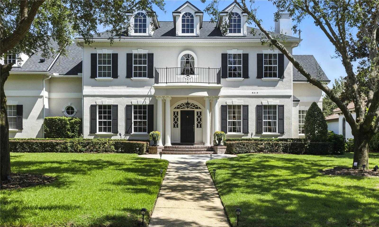 Experience the classic beauty and effortless living of this stately Southern 5-bedroom, 4.5-bathroom home designed for entertaining in the serene Northshore Village of Keene’s Pointe—a guard-gated golf and country club community.
Set among lakefront estates, this traditional Georgian Colonial-style residence, built by Stonebridge Homes, sits on a generous half-acre lot and exudes grandeur from the moment you arrive. A welcoming columned front porch leads into a gracious foyer, flanked by a refined library to the left and a formal living room with fireplace to the right. Continue through to discover a stunning music room large enough for a grand piano and an elegant dining room with French doors that open to a sparkling pool oasis.
Natural light pours in through Palladian windows, highlighting handcrafted woodwork, hardwood floors, and crystal chandeliers throughout. The butler’s pantry—with wine cooler and ice maker—connects seamlessly to an open kitchen that encompasses a spacious family room anchored by a brick fireplace. Nearby is the secondary staircase that leads to the upstairs media room/Pub-style Bar and the additional 4 bedrooms, while you will see the main floor guest ensuite (BR#5) located off the Family Room in its own wing for maximum privacy. A large bright breakfast area keeps everyone connected and offers direct access to the expansive screened pool and lanai.
Perfect for year-round entertaining, the outdoor living space features a covered sitting area, fireplace, and mounted TV—all under roof and adjacent to the enormous pool.
Upstairs, you’ll find four bedrooms including a luxurious primary retreat complete with its own fireplace, as well as a versatile media room everyone can enjoy.
Additional highlights include two oversized garages—one single bay ideal for a boat or large truck, and a separate two-car garage—both accessible from the rear of the home. A rare combination of classic elegance, flexible space, and value, this home has been meticulously maintained by current original owners and a new roof installed in 2022. A recent remodel/expansion of the home added some 600 sq ft of AC living space to the original plan. Public records are currently being updated to reflect that new amount.