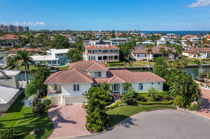 Perfectly positioned on a quiet cul-de-sac at the preferred south end of Longboat Key, this 4BR/5BA waterfront residence spans nearly 4,000 sq. ft. of beautifully designed living space just one lot from the open bay. The paver drive and lush landscaping create a gracious welcome to a home filled with natural light, soaring ceilings, and elegant architectural details. Expansive living areas flow seamlessly between spaces, featuring tile flooring, tray-accented ceilings, recessed lighting, and walls of glass framing tranquil water views. The open kitchen is ideal for entertaining, with stone countertops, white cabinetry with glass-panel accents, a breakfast bar, and direct access to the adjoining dining and living areas. The first-floor primary suite is a serene retreat, complete with rich wood floors, a spacious custom closet, pool access, and a luxurious bath with dual vanities, spa tub, and glass-enclosed shower. Upstairs, guest suites each offer en-suite baths for privacy and comfort. Outdoors, enjoy the resort-style pool surrounded by tropical landscaping and covered sitting areas. A private dock with 10,000-lb lift and seawall makes this a true boater’s paradise on a deepwater canal. Additional highlights include impact glass throughout and an oversized 3-car garage. Residents of Country Club Shores enjoy deeded beach access and the option to join the prestigious Longboat Key Club, offering 45 holes of championship golf, world-class tennis, a full-service marina, beachfront dining, fitness and spa facilities. All just minutes from St. Armands Circle and downtown Sarasota.