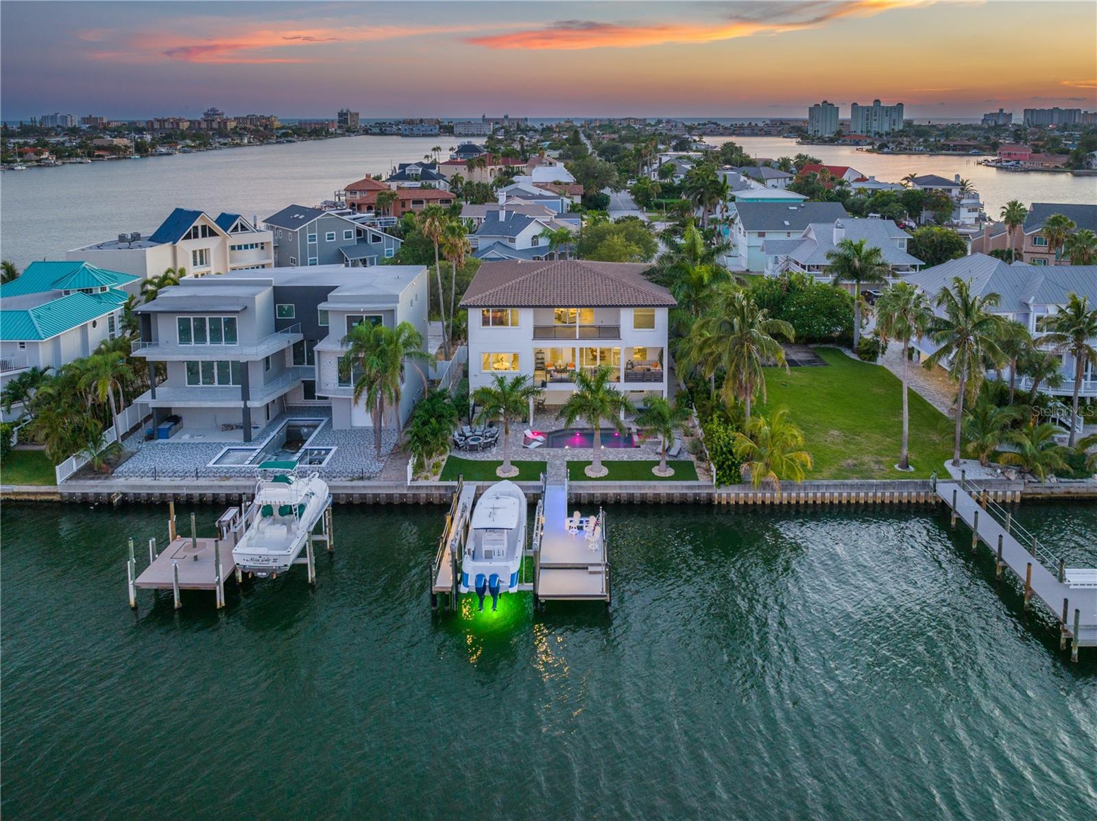 One or more photo(s) has been virtually staged. This exquisitely crafted three-level home, built in 2019, is located on the end of the charming beach community of Bahia Way in St. Pete Beach with wide open views of Boca Ciega Bay . The home showcases impeccable construction and features 4 bedrooms and 4.5 bathrooms that capture abundance of sunlight and water views. With 70 feet of water frontage, a brand-new dock with 30,000-pound, high speed, boat lift, offering both luxury and practicality for waterfront living. This residence offers a harmonious blend of modern design and coastal lifestyle with incredible desirable features, maintenance free landscape turf with grand brick pavers in both the front and backyard, high ceilings in every room, hardwood floors, an elevator (3-stop to all floors), a 6-car air conditioned garage with all new custom shelving & storage, all hurricane impact windows and doors, and a multitude of outdoor amenities. The home boasts an impressive kitchen with wood plank ceilings, two expansive islands, high-end appliances including a double oven, large refrigerator and freezer, two dishwashers, wine cooler, and double sinks. Additionally, there's a butler's walkthrough pantry and an oversized walk-in pantry for added convenience and providing a plethora of storage. The living room features tall accordion sliding doors opening to a spacious 432-square-foot patio with stunning views of Boca Ciega Bay, perfect for catching spectacular sunrises. The main level also includes a guest room with an ensuite bathroom, a half bathroom. and a den/office. Moving upstairs, you'll find a loft area that offers additional living space, a convenient laundry room for your daily needs, and two more spacious guest rooms, each thoughtfully designed with ensuite bathrooms. This layout provides both functionality and comfort throughout the different levels of the house. The third-floor owner's suite is truly expansive, featuring a breakfast bar, a spa-like bathroom equipped with double vanities, a luxurious garden tub, a shower adorned with multiple shower heads, and a balcony for a relaxing outdoor retreat. Outdoors, you'll find a glistening, heated Pebbletec pool & spa with LED lighting and water features, a plumbed gas fire pit for ample seating and a brand-new state of the art summer kitchen with an island equipped with a built-in audio system making it perfect for entertaining. Moreover, the property's location is exceptionally advantageous, providing easy access to public beach access, the renowned Don CeSar hotel, shopping, dining and the vibrant downtown area of St. Petersburg. This combination of lavish amenities and a prime location makes this home an exceptional find.
