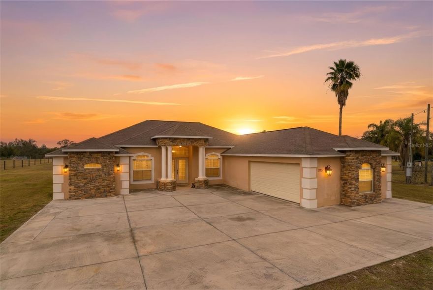 Set on just over 5 acres surrounded by open pastureland, this 3 bedroom, 2 bath home with a 2 car garage offers privacy, space and peaceful country living while remaining conveniently connected to nearby amenities. As you approach the property, an electric gate welcomes you into the fully fenced grounds leading to an expansive parking pad and a beautifully designed home featuring stone accents across the exterior. A covered front porch with soaring ceilings leads to double French front doors. Inside, elegant tile flooring with the look of polished marble flows throughout most of the home, excluding the 2 additional bedrooms. Immediately to the right is the formal dining room with a large window overlooking the front of the property while straight ahead the living room opens with sliding glass doors bringing natural light and views of the surrounding land. Moving further inside, the kitchen and breakfast nook feature a panoramic window and additional sliding glass doors framing views of the backyard. The kitchen is designed for everyday living and entertaining with a large breakfast bar, built-in shelving, granite countertops, dark wood cabinetry, stainless steel appliances, dual sink, and spacious pantry. Beyond the kitchen, a wide arched opening framed by decorative columns leads into the family room where a tray ceiling adds architectural detail and a large arched window fills the space with natural light. The primary suite is located on the left side of the home for added privacy and features marble-look tile flooring, a tray ceiling, sliding glass doors to the rear patio and two additional windows overlooking the acreage. The ensuite bathroom features cathedral ceilings, a centrally positioned soaking tub and a large walk-through shower accessible from both sides with dual shower heads, a rainfall shower head, built-in shelving and a window for natural light. Granite countertops and dark wood cabinetry complement the space while the vanity provides extended counter area. Just beyond, the walk-in closet includes built-in storage and a window. On the opposite side of the home are two additional bedrooms separated by a hallway bathroom. Both bedrooms feature carpet flooring, a window, and a built-in closet. The shared bathroom includes granite countertops, dark wood cabinetry, a single vanity, and a tub/shower combination. Near the dining room is the laundry room with corridor access to the garage, built-in shelving, a utility sink, and washer and dryer. At the rear of the home, the patio offers a spacious outdoor living area that is mostly covered and extends into an open sun patio, providing space for relaxing or entertaining while enjoying views of the backyard and surrounding acreage. The property also includes a separate fenced pasture area suitable for farm animals such as horses, cattle, chickens, and goats. The land offers room for gardening, recreation, animals or future additions while maintaining privacy and wide-open views. Located in Brooksville, the home provides convenient access to the Suncoast Parkway for travel to Tampa and surrounding areas including shopping, dining and Tampa International Airport. Nearby attractions include Weeki Wachee Springs State Park for kayaking and paddleboarding in clear spring waters, Withlacoochee State Forest with miles of trails for hiking, biking and horseback riding and historic downtown Brooksville known for local shops, restaurants, festivals, and community events.