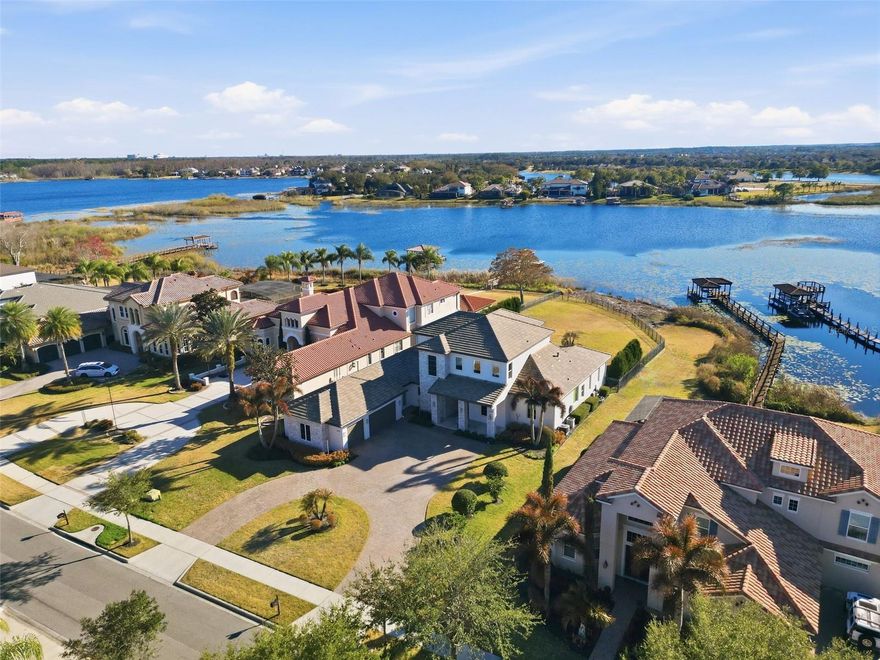 Luxury meets laid-back lake living on Lake Hancock in Winter Garden, inside the sought-after Independence community with parks, trails, and a true neighborhood feel. Custom built by Brierhill Homes, recognized as MCBC Builder of the Year, and professionally designed/furnished by Gilmore Design Co., this exceptional direct lakefront residence sits on one of the area’s largest lots—with an oversized, fully fenced backyard—perfect for entertaining—where you can enjoy stunning sunsets over the water and catch the Disney fireworks on select nights. Arrive via an impressive circular drive and step into a striking entry featuring a custom front door, polished natural stone flooring, and a dramatic stone accent wall—framed by a deep, covered front porch with a rich wood-plank ceiling that immediately sets the tone. It’s a welcoming space that’s perfect for a small seating area to enjoy morning coffee or greet guests in style. Inside, the home is bright, elevated, and designed for both entertaining and everyday comfort, highlighted by a timeless coastal-modern palette with white oak flooring, a beautiful white oak staircase with integrated LED lighting under each step, and custom ceiling details throughout (including soffit/tray accents and integrated lighting). The layout offers 5 bedrooms, each with a private en-suite bathroom and walk-in closet, and each bedroom includes blackout honeycomb shades for comfort and privacy—including a stunning first-floor primary suite with serene lake and backyard views, plus a dedicated first-floor guest suite. You’ll also love the private office and a media room that easily works as a flex space (playroom, gym, second lounge, or homework room). At the heart of the home, the chef’s kitchen showcases Thermador appliances and a show-stopping double island topped with Cambria quartz with subtle gold veining, plus a custom chevron-designed backsplash with under-cabinet LED lighting that highlights the detail beautifully. The kitchen flows seamlessly into the main living space for true indoor-outdoor living. A wall of living room sliding glass doors opens wide, creating one expansive space that connects the interior to the lanai, pool, and lake beyond. Enjoy built-in Sonos sound in the living room and kitchen, with audio extended to the outdoor kitchen as well—plus the flex/media space is pre-wired if additional speakers are desired. The living room also features a sleek gas fireplace framed in natural stone, flanked by custom built-ins for a clean, designer finish. Out back, unwind in your private retreat with a heated pool and spa, generous covered areas, and a summer kitchen made for sunset dinners. The first-floor lanai (including the summer kitchen) and the second-floor balcony are both fully encapsulated with motorized screens controlled by remote—perfect for effortless, bug-free evenings and both outdoor living areas feature a warm wood-plank ceiling accent that brings a high-end, resort feel. Additional highlights include a whole-home water softener/filtration system (low/zero maintenance), a built-in security system with exterior cameras, built-in Sonos audio, and whole-home smart lighting with keypad controls and scene presets—plus an oversized 3-car garage. Select furniture may be purchased separately upon request.