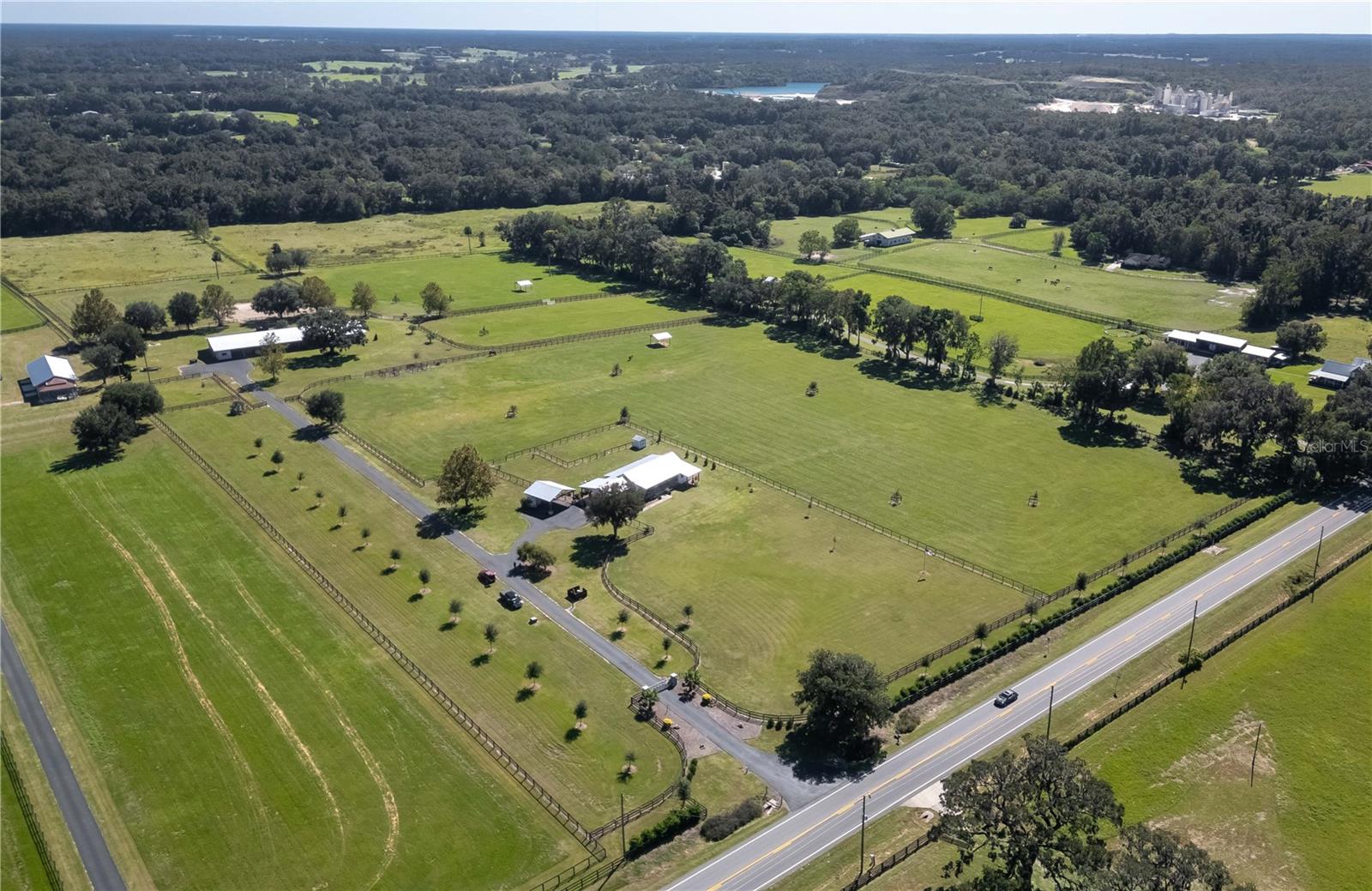 Amongst established horse farms in Marion County’s quiet countryside, this 21+ acre farm– which can be divided– is an immaculately maintained option for passionate equestrians. High and dry, the property features lush pastures with gentle roll, wide open spaces gently dotted by mature oaks, and underground utilities that keep the natural beauty of the property intact. Fenced and gated, the property is nicely private and features brand new fencing. A long tree-lined paved drive leads to the inviting home and continues back towards the large shed-row style barn. Perfect for equestrians of multiple disciplines, the barn features a total of 19 stalls, equipment storage, and a fully renovated multi-story barn apartment. Several well-designed paddocks with brand-new fencing and an updated layout provide ample space, while a dedicated riding ring enhances training opportunities. The 2-bedroom, 2.5-bath home is a tasteful dog-trot style construction that has been elegantly remodeled. The home has plenty of curb appeal with tasteful landscaping and a large covered front porch that provides ample space for seating, while the interiors feature high ceilings throughout and a split-bedroom floor plan that ensures plenty of privacy. The kitchen is well-appointed for those who enjoy cooking, with stainless steel appliances including a matching vent hood, lots of cabinet storage, tiled backsplash, a large center-island with stack-stoned detailing, and an additional pantry. Directly open to the kitchen is the living area, which includes a stunning floor-to-ceiling decorative stone electric fireplace and lots of natural light. The primary suite is a particularly attractive option with a larger layout, direct access to the patio via a set of french doors, a huge walk-in closet, and a private en-suite bathroom with dual vanities, garden tub, and a spacious walk-in shower. A huge covered back patio looks out to the barn and nearby pastures, providing the perfect place to enjoy a quiet cup of coffee or enjoy an informal meal in the warmer months. For added convenience, the home is equipped with a whole-home generator, ensuring uninterrupted power no matter the season. Attached to the home via a covered breezeway is a separate studio that could be used as a private office, hobby area, private suite, or anything in between. Separate from the home is a covered carport area that could be used as a separate entertaining space if preferred, with tongue and groove ceilings, ceiling fans, and added storage space. Both the World Equestrian Center and HITS are just a scenic 20 minute drive from the farm, opening up year-round competition and spectating opportunities. Downtown Ocala and Gainesville are both roughly 30 minutes from the farm, providing abundant shopping, dining, entertainment, and medical options in both areas. If you’re on the hunt for your perfect slice of Central Florida horse country, be sure to schedule a showing today!