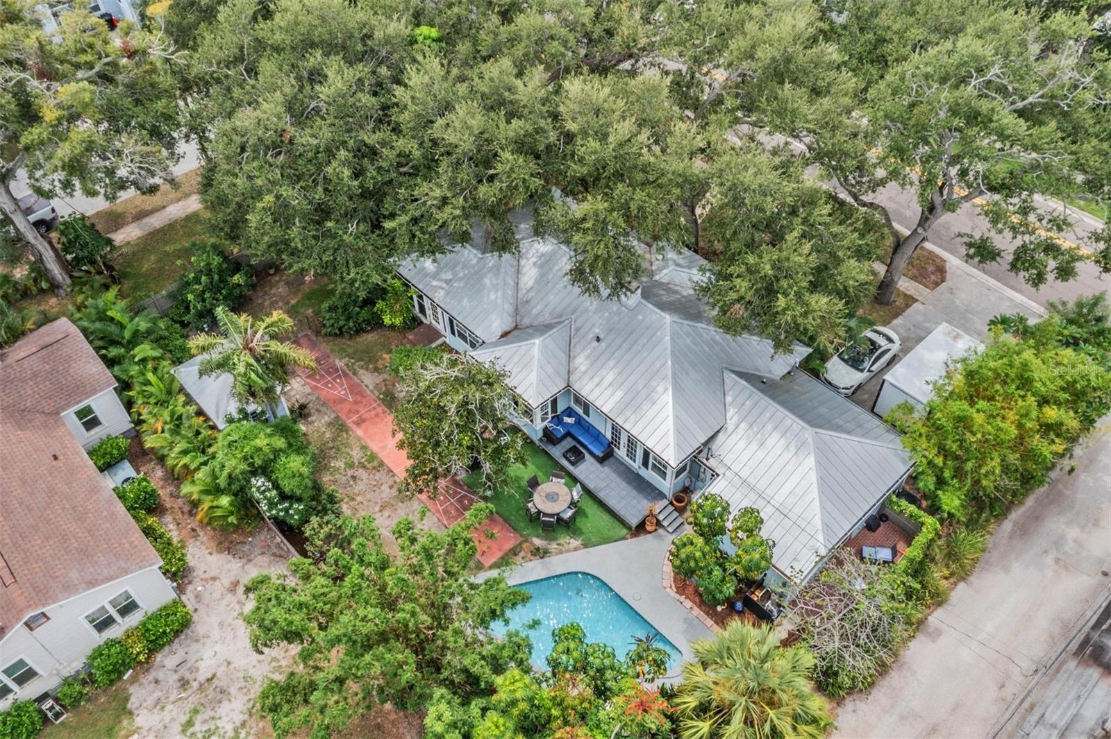 Live, Work & Play in Historic Kenwood! Get ready for poolside fun and shuffleboard nights—this charming home is made for entertaining and relaxation. The garage has been smartly converted into a private master suite, offering a true retreat or the perfect guest space for overnight visitors. Sitting on a massive double lot surrounded by lush greenery, this home feels like your very own private oasis, with plenty of room to build the garage of your dreams. Inside, you’ll love the warmth of original hardwood floors, classic cove ceilings, and a stylish gas kitchen designed to bring out your inner chef—complete with a new gas range. A newer metal roof adds peace of mind and long-lasting protection. Step outside to enjoy your private escape: a shed with a metal roof and electricity, 1943-stamped shuffleboard, poolside lounging, and well water irrigation to keep your lush landscaping thriving. Important updates bring additional value and ease of ownership: both AC units (2025), irrigation pump (2025), electric panel (2025), and gas range (2025), pool pump and vacuum (2023). Located in the heart of Historic Kenwood—an Artist Enclave community where you can live, work, and sell your art from home—this gem requires no flood insurance and puts you just minutes from vibrant downtown St. Pete and a quick 15-minute drive to the beaches.
Fun fact: Founded in 1924, the St. Petersburg Shuffleboard Club is the oldest and largest shuffleboard club in the world—making this home’s shuffleboard court an iconic nod to local history!
Privacy, character, updates, and unbeatable location—this home has it all!
