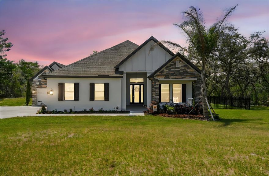 Luxury Meets Livability on 4.24 Acres in the Gated Equestrian Community of Bella Terra. Welcome to this exceptional 2024-built estate home in the serene, gated equestrian community of Bella Terra in Hudson, Florida. Set on 4.24 acres that is mostly fenced, this 4-bedroom, 3-bathroom residence blends upscale finishes with the flexibility of large land ownership. With builder warranties still in place, this nearly new home offers luxurious upgrades, generous space, and long-term peace of mind. A spacious front porch leads to an 8’ glass entry door flanked by sidelights and a transom. Inside, the grand foyer with crown moulding introduces a thoughtfully designed interior featuring 8’ interior doors, 5.25” baseboards, and luxury vinyl plank flooring throughout the main living areas. The formal dining room flows into a dramatic family room with a custom-built stone accent wall, electric fireplace, and mantle with TV mount. French doors open to a covered lanai with sweeping views of the property. The outdoor kitchen, with granite counters, sink, grill, and storage, is perfect for entertaining. The chef’s kitchen features a massive peninsula with seating, quartz countertops, Arabesque tile backsplash, soft-close cabinetry with crown moulding, and stainless steel smart appliances, including a 5-burner cooktop and range hood. A walk-in pantry with custom shelving, butler’s pantry/drop zone, and built-in cabinetry in the dining nook and laundry room enhance everyday functionality. The private primary suite boasts a recessed ceiling, double crown moulding, a custom shiplap fireplace wall, and large windows with tranquil views. The luxurious en suite bath includes a freestanding soaking tub, walk-in shower, dual vanities, water closet, and an oversized custom closet. Bedrooms 2–4 are generously sized. Bedroom 2 offers en suite-style privacy via a vestibule, while Bedrooms 3 and 4 share a Jack-and-Jill bath with individual vanities. A large media room with coffered ceiling and double doors provides flexible space for a home theater, studio, or game room. Additional features include double-pane tilt-out windows with blinds, hurricane shutters, reverse osmosis system, water softener, and an oversized laundry room with abundant cabinetry and quartz counters throughout. The home offers a split 2-car and oversized 1-car garage with EV charging readiness and an extended driveway. Outdoors, enjoy mature trees and dual fencing—one for daily use, and another enclosing the much of the remaining acreage. Zoned for equestrian use, the property allows BARNS, STABLES, WORKSHOPS, or GARAGES. Over 6 miles of community riding trails—including one directly behind the home—make this a dream for horse lovers. A SafeTouch security system with cameras adds peace of mind. Bella Terra offers golf cart-friendly roads, wide-open green space, and peaceful living—while still providing quick access to US-19, the Suncoast Parkway, and all that Pasco County offers. Enjoy nearby parks, trails, golf, and coastal recreation. Here, you’ll find the ideal blend of quiet country charm and convenient access to Tampa’s top beaches, shopping, and business centers. Don’t miss this opportunity to own a luxury home on acreage in one of Hudson’s most distinctive gated communities—where land, luxury, and lifestyle converge.