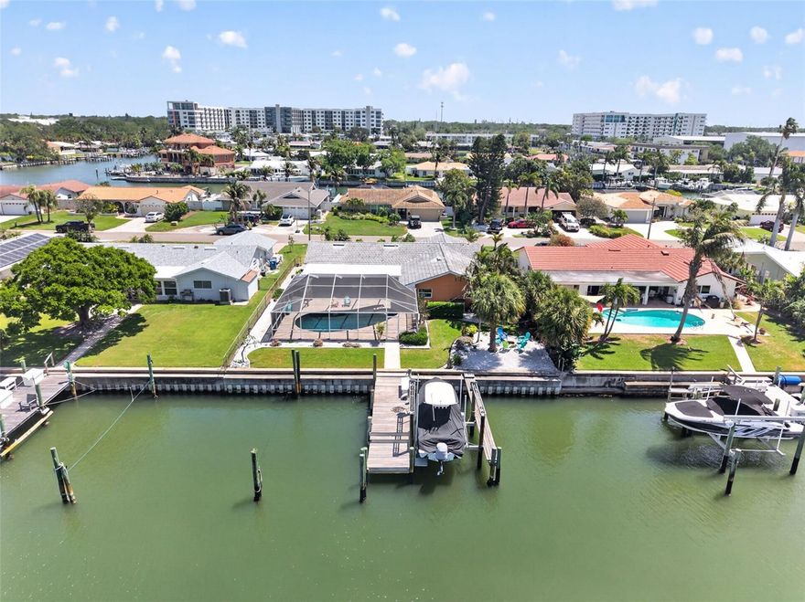 Stunning waterfront home nestled in the serene Broadwater neighborhood, offering 80 feet of seawall on wide, deep-water canals with direct access to Boca Ciega Bay and the Gulf beyond. Exceptionally high bridges allow larger boats to clear with ease, making this a true sailboat-friendly property.
This beautifully updated and well cared for 4 bedroom, 2 bath block home features a desirable split floor plan with separate living and dining rooms plus a spacious family room. Clean lines, tasteful décor, and abundant natural light enhance the inviting mid-century modern interior. The kitchen offers breakfast bar seating, excellent flow to the family and dining rooms, pocket sliders, and picturesque views of the pool and saltwater canal from the sink.
Outdoor living is a highlight, with a screened pool patio featuring a cypress-lined covered porch ceiling and a cedar gazebo, perfect for enjoying sea breezes and sunset views. A fire pit area sits off to the southeast of the home, creating an ideal waterfront gathering spot. The newer seawall, private dock, boat lift, and additional boat slip complete this boater’s paradise.
No flooding during past hurricanes and buried power lines add to the peace of mind.  Added wire lath with additional vapor barrier under the wire lath and stucco reinforces the already sound structural integrity of the home, while mature landscaping frames the property beautifully. Paddleboard through the canals to Gulfport or enjoy quick water access to Boca Ciega Bay. A short walk, bike ride, or boat ride brings you to Tiki Docks for waterfront dining or to Maximo Marina.
Ideally located just 5 minutes from the Don CeSar and Pass-a-Grille Beach, less than a mile to I-275, 4 miles to Gulfport, 6 miles to vibrant downtown St. Petersburg, and 8 miles to Fort De Soto Park, this exceptional waterfront home delivers the very best of Florida coastal living.