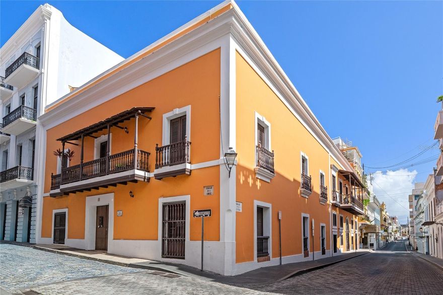 Set within a beautifully restored historic building in the heart of Old San Juan, on the corner of Cruz and Luna streets, this second-floor apartment offers architectural grandeur and everyday convenience.  Just one block from Plaza de Armas and mere steps from La Cochera parking garage, grocery store, pharmacy, and neighborhood café, the location is truly exceptional—immersed in the rhythm of the old city while effortlessly practical for daily living.  Inside the building, wide entryways, soaring ceilings, exposed ausubo beams, and a gracious staircase reflect the craftsmanship and elegance of a bygone era, impeccably maintained.  

Beyond striking wood double doors, the apartment unfolds beneath dramatic 18-foot ceilings that immediately evoke old-world Spanish charm.  The unit is interior-facing, opening onto a beautifully landscaped central courtyard garden below—creating an atmosphere of remarkable quiet and privacy, entirely removed from the street and city sounds outside.  Living and dining areas, along with the hallway leading to the bedrooms, are lined with tall louvered windows overlooking a central courtyard, allowing natural light and cooling breezes to circulate throughout the space.  A bright hallway punctuated by graceful Gothic arches leads to the private quarters, enhancing the sense of quiet refinement and architectural continuity.  

The layout is both elegant and functional.  The kitchen offers space for a breakfast nook and includes a mezzanine loft ideal for storage or a compact office.  The primary suite is defined by tall double doors, a serene bedroom, walk-in closet, and ensuite marble bath, while the secondary bedroom also enjoys generous proportions, high ceilings, and its own walk-in closet.  Offered unfurnished, the apartment includes all appliances, ceiling fans, and air-conditioning units that comfortably cool the entire residence, and a 200-gallon cistern exclusive to this unit—an inspired Old San Juan home where history, beauty, and livability coexist seamlessly.