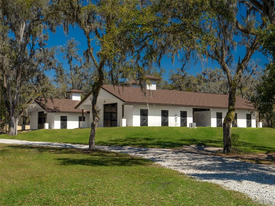 This 26.67-acre property, featuring stunning live oaks and magnolias, is a prime opportunity for equestrian enthusiasts seeking both privacy and convenience! Located just 5 minutes from HITS and 15 minutes from the World Equestrian Center, it boasts a high-end, 20-stall H-style barn with 12,050 sq. ft. of finished space. The barn includes spacious aisles, rubber pavers throughout, fans, sliding front stall doors, and rear Dutch doors, along with two air-conditioned tack rooms and a feed room. Additional amenities include 8 grooming/wash stalls, a 150'x250' Wordley Martin riding ring with irrigation from a dedicated well, and a cement curb along the perimeter. The barn also features a kitchenette with granite countertops, a dishwasher, refrigerator, and microwave, as well as an adjoining bathroom. A large laundry room with dual hookups and ample cabinet space further enhances convenience. Plans for a custom 5,886 sq. ft. home by Rispoli Architects are also included. The property is fully fenced, with options for paddocks and outbuildings, offering the perfect balance of seclusion and easy access to top equestrian facilities. NW 115th St is a private, paved dead-end road, lined with newer horse farms on parcels of no less than 10 acres each, and Spectrum has recently installed cable for both internet and cable services, adding to the property's appeal.
