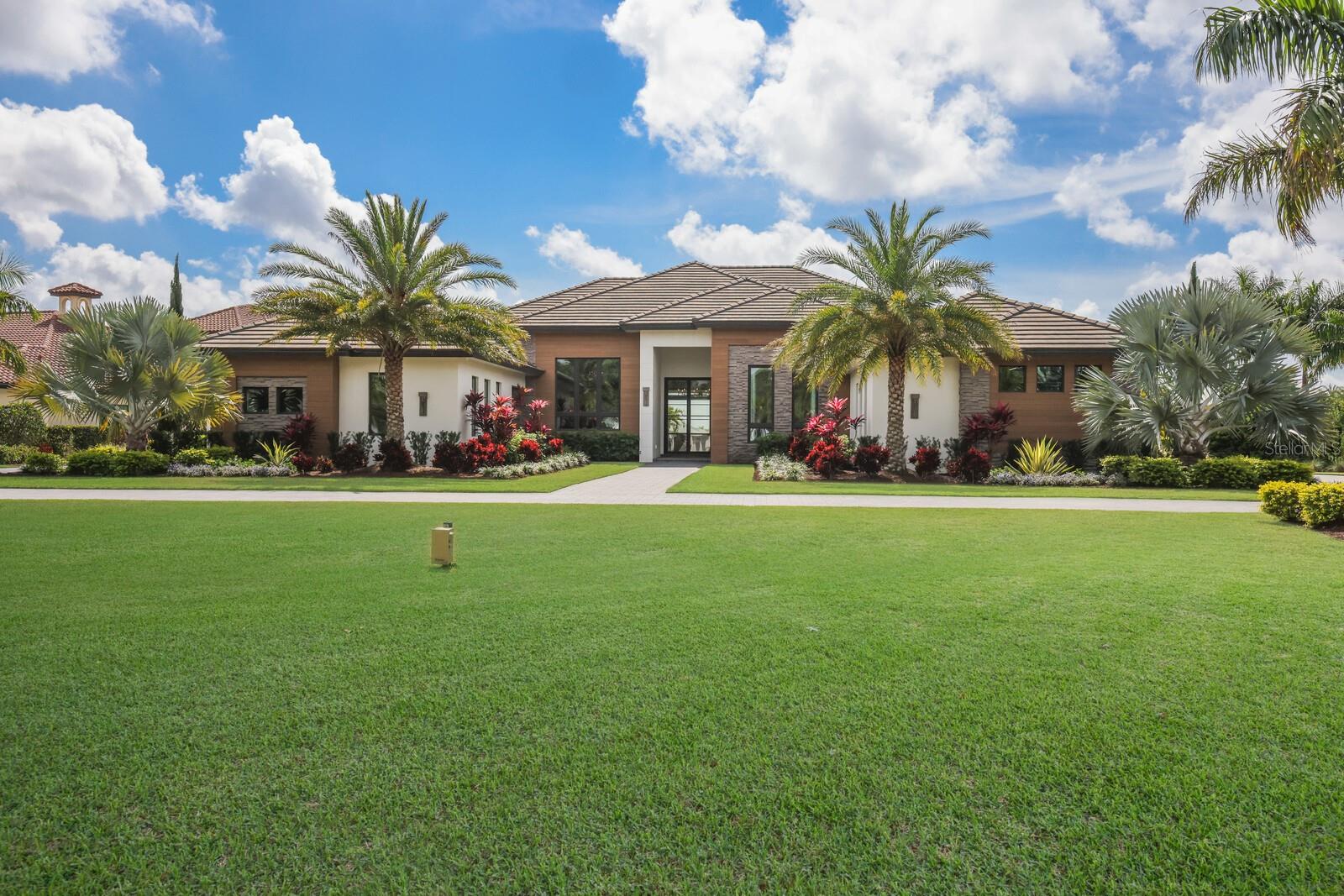 Designed with a nod to the modern movement of architectural styles and positioned on a scenic 1.71 acres in the exclusive and sought-after gated community of The Concession, this residence showcases clean lines, exceptionally planned indoor-outdoor spaces, and the latest in smart home technology. Voted “Best Overall Home” by Parade of Homes in 2021, the former Newcastle model was built by John Cannon encompassing 4,814 square feet of generously proportioned one-story living including private casita, and an expansive outdoor retreat encompassing 2,806 sqft screened lanai with extensive open and under cover spaces grounded with deep gray slate pavers, soaring accent ceilings, full summer kitchen, lounging chaise deck, putting green, fire pit, PebbleTec heated saltwater pool/spa with sun shelf, panoramic clearview screen, and a separate nature viewing deck to enjoy the lake views beyond. 10' accordion-styled impact glass walls with black iron horizontal lines seamlessly connect the resort-styled outdoor living space to a grand great room with sumptuous hardwood flooring, gas fireplace and stunning beam-accentuated ceilings. Dinner guests are treated to an open feel surrounded by disappearing cornerless glass doors and an all-glass temperature-controlled wine room with backlit agate accent wall. Meanwhile chefs will delight in the oversized kitchen with show-stopper sized windows, two separate marble islands, Albrecht wood cabinetry, a hidden pantry with built-in cabinetry, and all high-performance appliances. An impressive club room directly off lanai beckons for entertaining complete with built-in beverage center, luxuriant ceiling design and direct access to an open courtyard. Relax and unwind in the owner’s quarters positioned on a private wing, offering a spectacular ceiling treatment, large scale windows overlooking the lake, direct lanai access, two oversized walk-in customized closets, and a luxuriously appointed bath with two separate vanity station wings anchored by an oversized all-glass dual entry shower at its center, a jetted tub surrounded by walls of glass looking into a private courtyard with outdoor shower, and even two separate water closets. The private casita off the lanai is optimal for guests with its own morning bar, walk-in closet, private full bath, volume beamed ceiling and stunning views. On a separate wing of the home there are two additional guest suites generous in size, both with walk-in closets and connected to private full baths. The residence also offers an impressive office behind double-entry doors with elevated step up area, built-in shelving and accent sconce lighting. Other notable highlights of this 7,704 total square foot residence includes a brilliantly located laundry room with cabinetry, sink, and desk area, Navien tankless water heater, built-in mudroom area, a dual split side load 4-garage, one with an air-conditioned wall unit, and Control4 home automation and networking system unifying lighting, audio, video, climate control, and security. This bespoke offering defines modern refinement beckoning a lifestyle fulfilled in this renowned community infamous as the home to the World Golf Championship PGA golf tournament in February 2021, to the World Champions Cup in December 2023, and to its striking oak hammocks, pines and large lakes, all near dining, shopping, polo, events in the vibrant Lakewood Ranch and UTC area, yet still nearby to the enriching culture and beaches of Sarasota