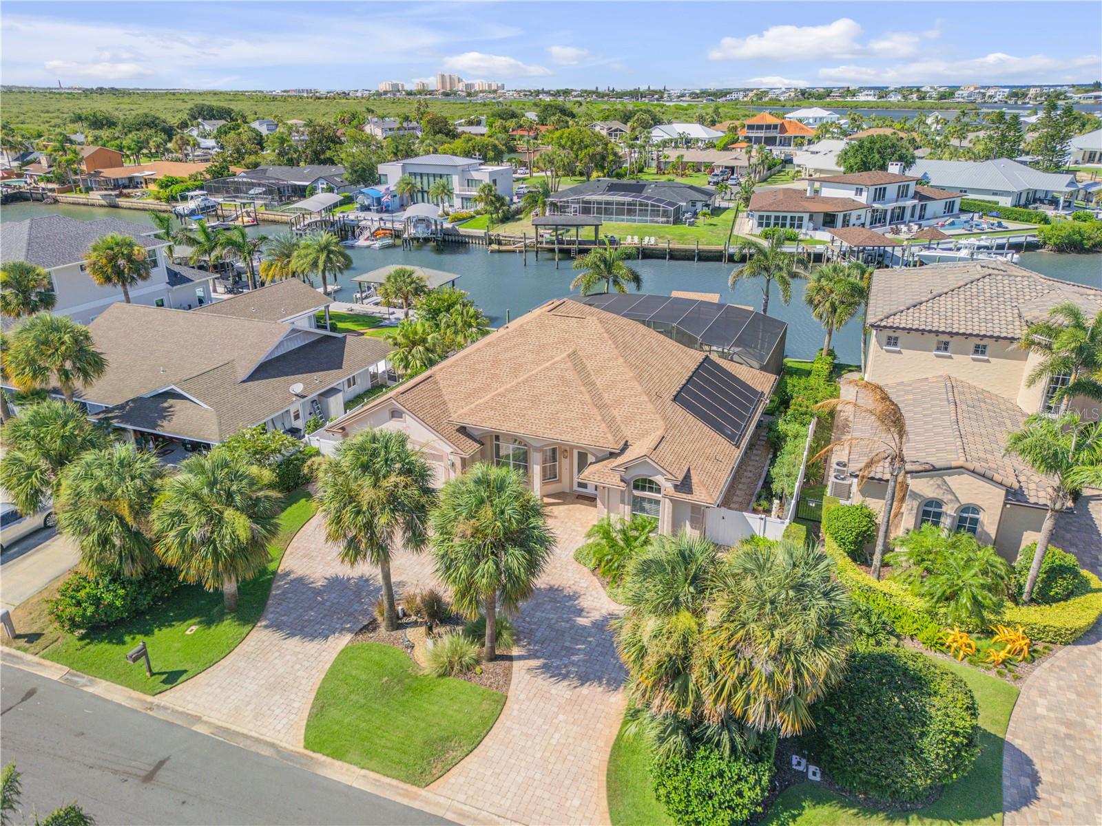 Live the Dream at 133 Via Capri –Where Elegance Meets Coastal Luxury
Every detail of this extraordinary New Smyrna Beach estate has been curated for those who demand excellence, style, and seamless indoor-outdoor living. From the moment you arrive, a sense of grandeur unfolds—twin glass-panel doors open to reveal soaring 12-foot ceilings, custom tile inlays, and designer lighting that set the tone for the elegance within.
This isn’t just a home—it’s a private resort, a showpiece of craftsmanship and innovation, where architectural beauty meets top-tier functionality.
Step into the expansive great room, where floor-to-ceiling windows draped in luxurious fabric flood the space with natural light, framing views of your private pool oasis. Centered around an 80-inch ‘Modern Flames’ recessed fireplace and illuminated by sleek LED and swivel downlighting, this open-concept living space flows effortlessly into the gourmet kitchen and outdoor entertainment areas.
The chef’s kitchen is a triumph of German design, anchored by SieMatic custom cabinetry with high-gloss and wood-grain finishes, stainless steel drawers, and premium Miele appliances—including multifunction, steam, and speed ovens, a concealed refrigerator/freezer, induction cooktop, and wine storage. A stunning quartz island with breakfast bar seating, a granite sink, and pendant LED lighting make it both a centerpiece and a culinary workspace.
The primary suite is a sanctuary, with private access to the lanai, his-and-hers walk-in closets, and a vaulted dressing/exercise space leading into a spa-like bathroom. Frameless glass shower enclosures, LED-lit mirrors, rain showerheads, and designer finishes create an atmosphere of indulgence.
Guest accommodations continue the luxury experience, with a fully tiled bathroom, sleek vanity, glass accents, and built-in seating in the shower.
Step outside to your personal paradise: a travertine-tiled lanai with a saltwater pool and spa, complete with sundeck, waterfalls, and a bubbler jet, all controlled by an I-Aqualink system and secured with hurricane-grade electric roller shutters. The fully equipped summer kitchen with granite counters, built-in grill, searing burner, cooler, and bar seating for six is the ultimate space for entertaining.
For boating enthusiasts, the waterfront amenities are unrivaled: an under-roof lift for boats over 25’, a fixed dock for vessels over 45’, and a floating dock accessible via an aluminum gangway enhanced with lighting and surveillance for peace of mind.