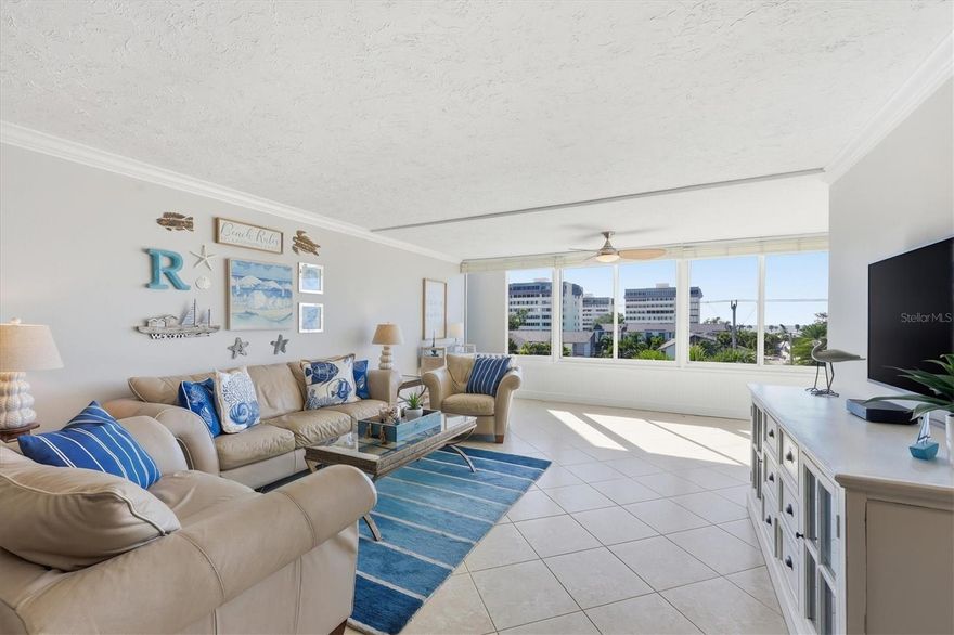 Set within Peppertree Bay on Siesta Key, 1200 E Peppertree Lane #307 offers a well-proportioned, turnkey, move-in ready two-bedroom, two-bath residence encompassing 1,466 square feet. The interior presents a bright, open layout anchored by a spacious great room, where crown molding, tile flooring throughout, and an expansive wall of impact glass windows create an airy, light-filled living environment. The adjoining dining area flows seamlessly into the kitchen, reinforcing the home’s functional, connected design. The kitchen features a tray ceiling with inner crown molding, recessed lighting, abundant wood cabinetry, granite countertops, a tile backsplash, and a full suite of stainless-steel newer Whirlpool appliances. A breakfast bar provides additional prep and serving space, supporting both everyday living and casual entertaining. The primary bedroom is generously scaled and benefits from strong natural light, crown molding, a walk-in closet, and direct access to the enclosed sunroom. The primary bath includes a granite-topped vanity, glass-enclosed walk-in shower, linen storage, and updated fixtures. A well-sized guest bedroom with an oversized window alcove and a nearby full bath maintains privacy and flexibility for visitors. An enclosed sunroom lined with windows extends the living space, offering versatility as a lounge, office, or secondary sitting area. A stacked washer and dryer are conveniently positioned within a dedicated closet. Newer HVAC system (2024) and Water heater (2025).  Peppertree Bay is a Gulf-to-Bay community providing private deeded beach access, a fishing pier, two resort-style heated pools, clubhouses, a fitness center, saunas, tennis and pickleball courts, covered under building assigned parking with this unit that provides a bicycle rack and unit storage, and multiple outdoor gathering areas. This building has newer elevators along with stairwell access, with the building roof being replaced in 2020. The location places residents directly on Siesta Key, home to Siesta Beach, consistently ranked the #1 beach in the United States by TripAdvisor, further underscoring the appeal of both the setting and lifestyle offered by this residence.